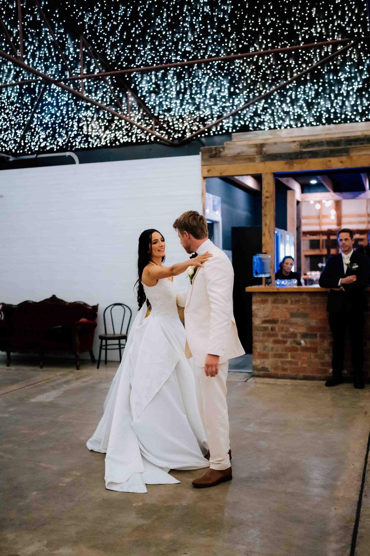 Bride and groom share their first dance under twinkling fairy lights at an elegant indoor wedding reception.