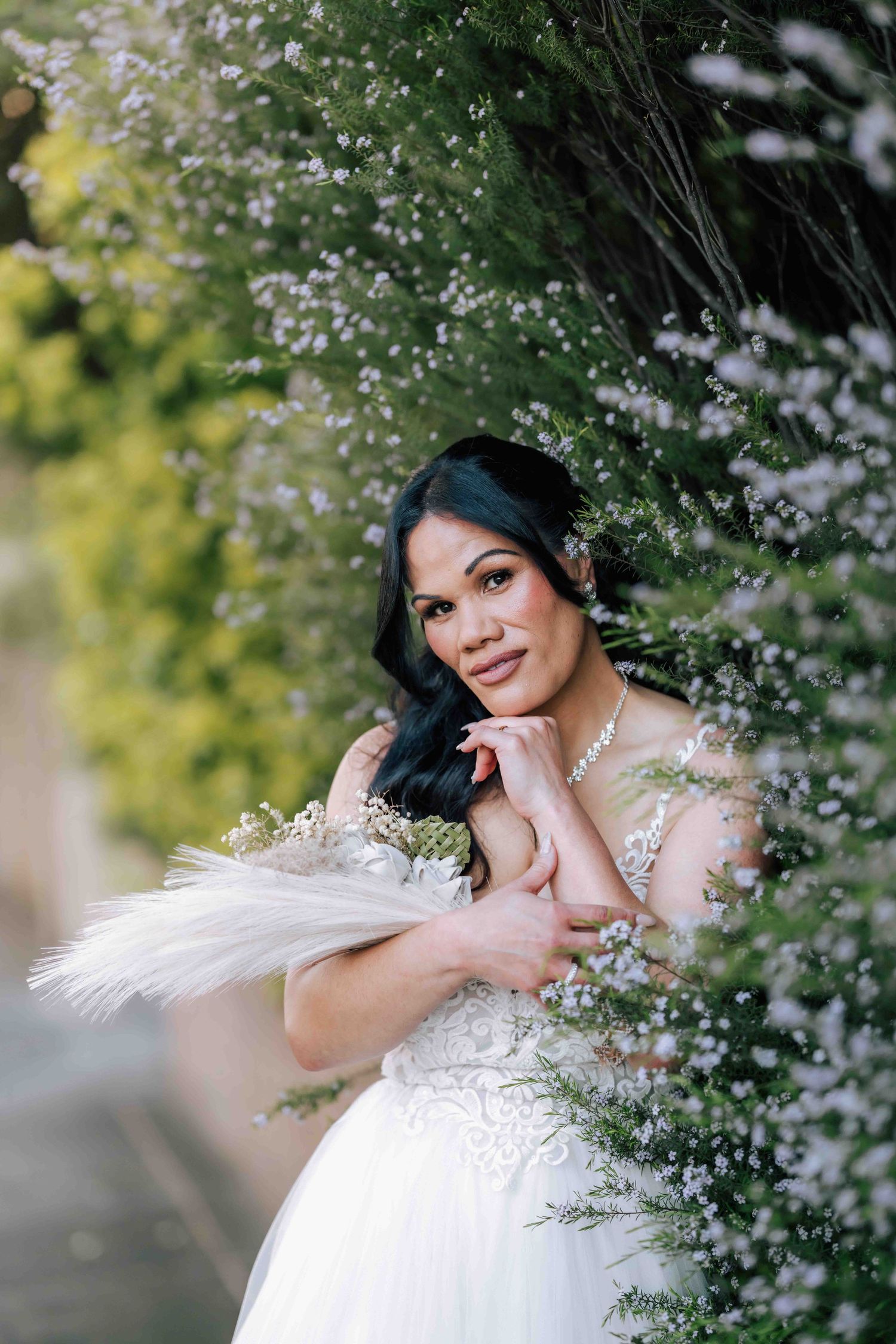 Beautiful bride in lace wedding gown holding feather bouquet among white blooms.