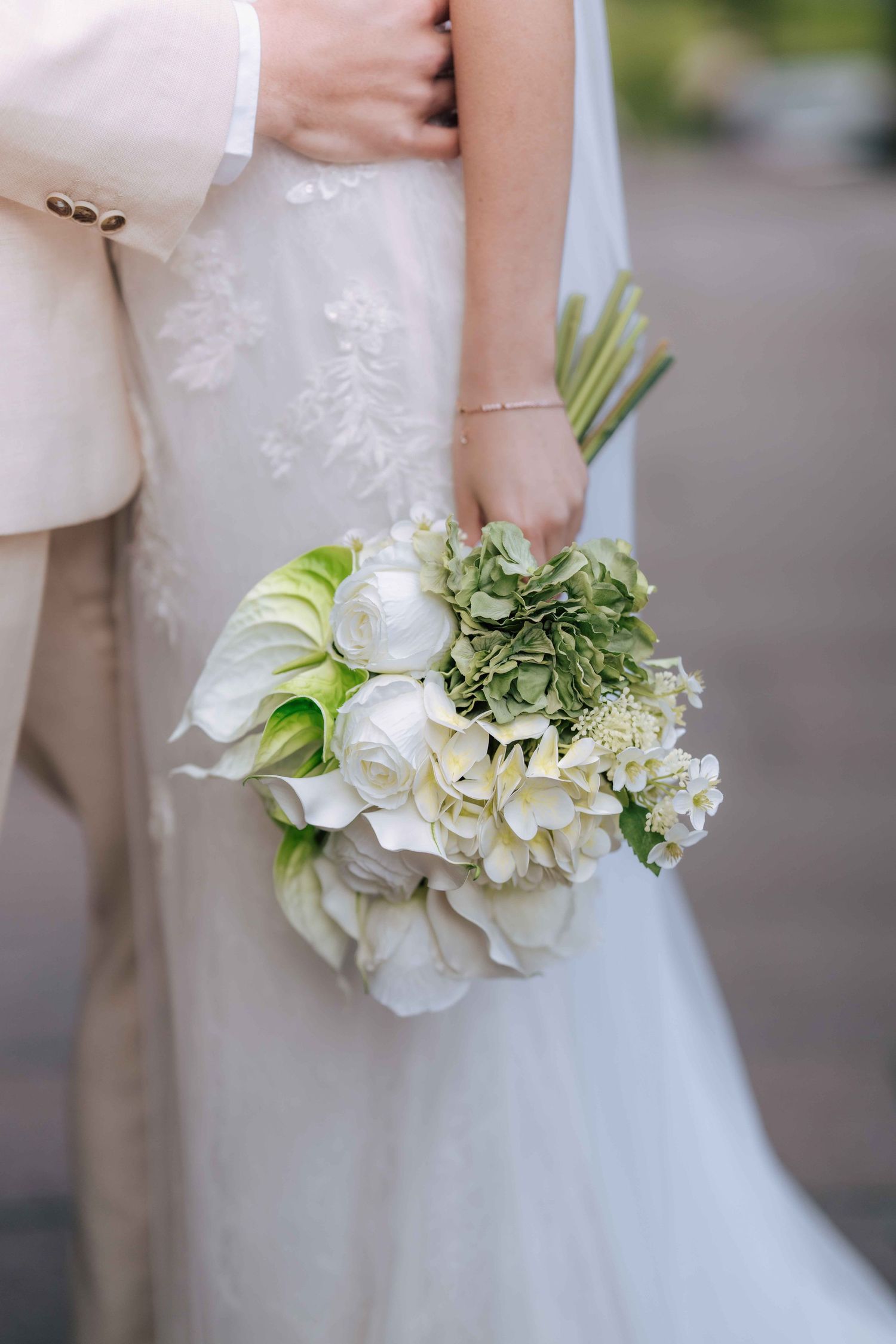 Bride holds lush white and green bouquet with tulips and hydrangeas in wedding dress.