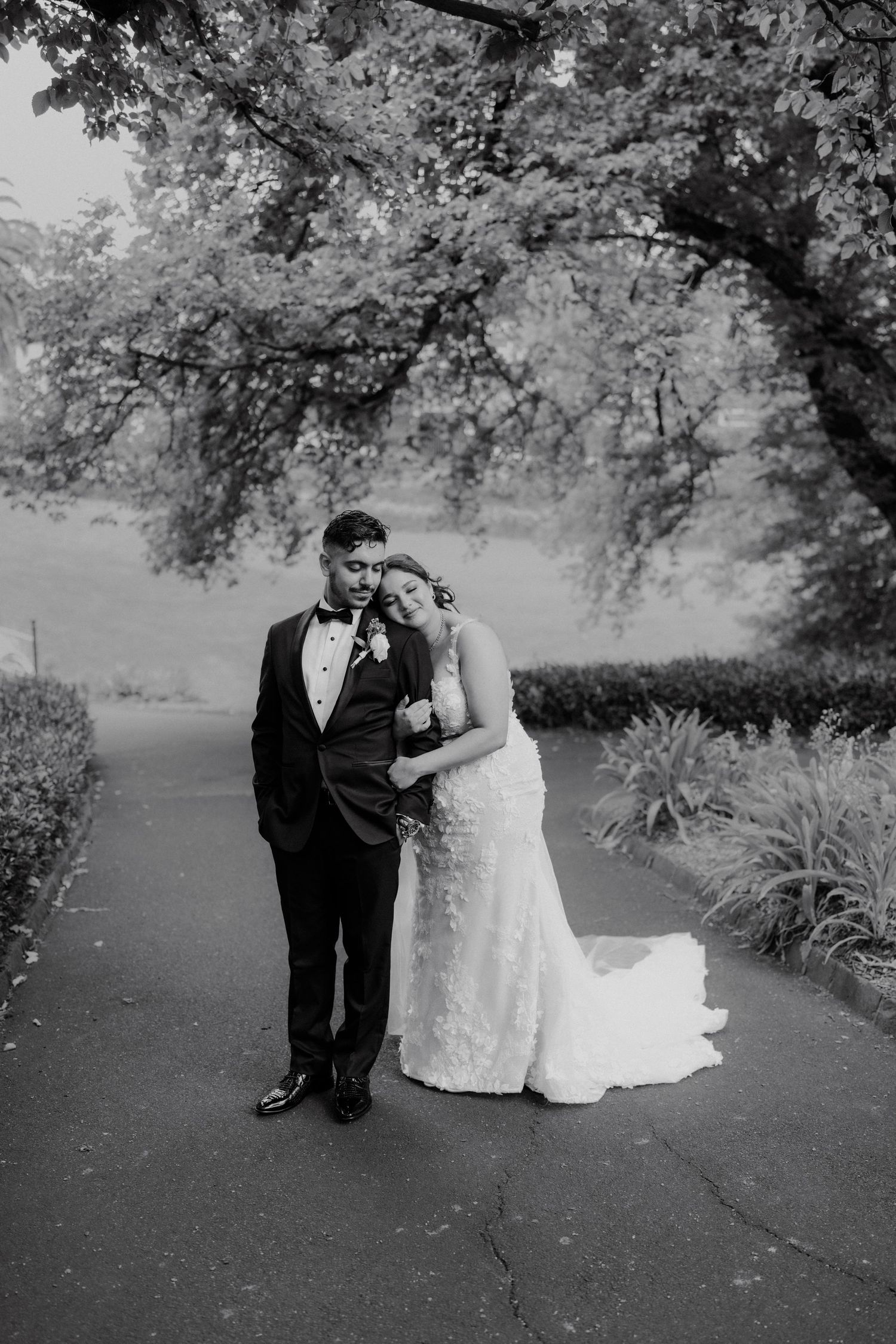 Black and white portrait of bride leaning on groom on a garden pathway.