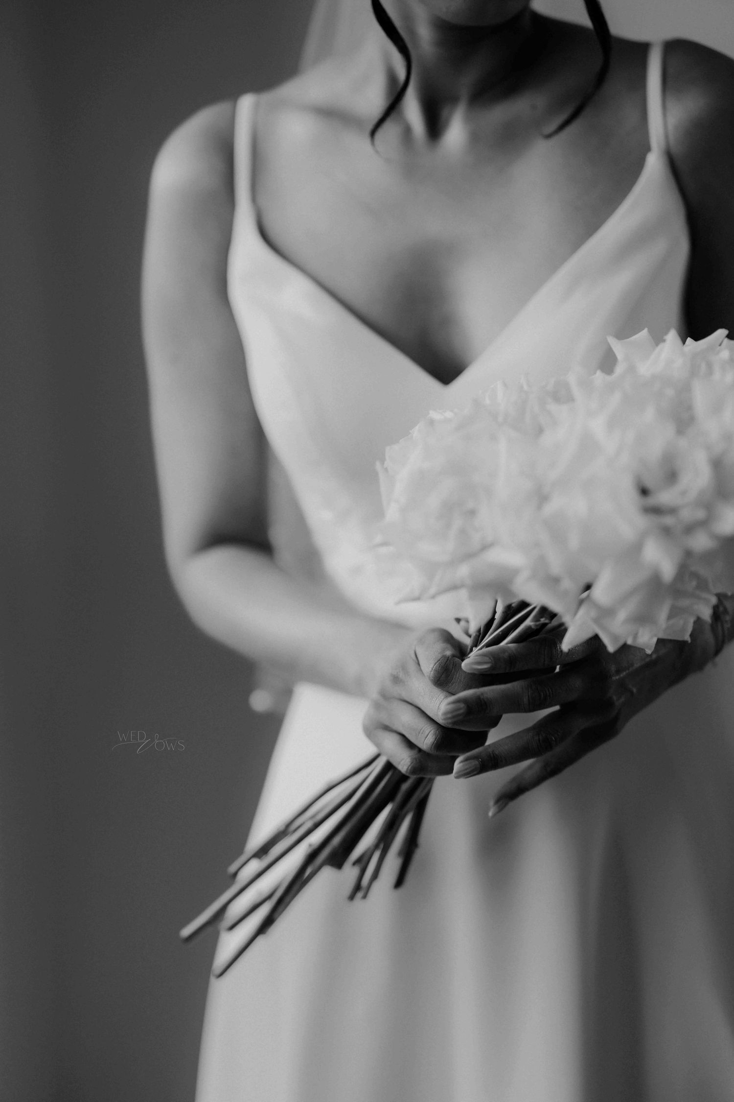 Black and white close-up of bride in spaghetti-strap gown holding a lush white peony bouquet.