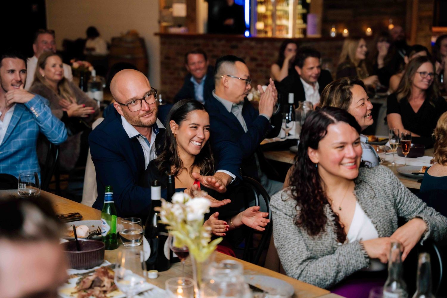 Wedding guests laugh and enjoy drinks while seated at decorated tables during reception dinner.