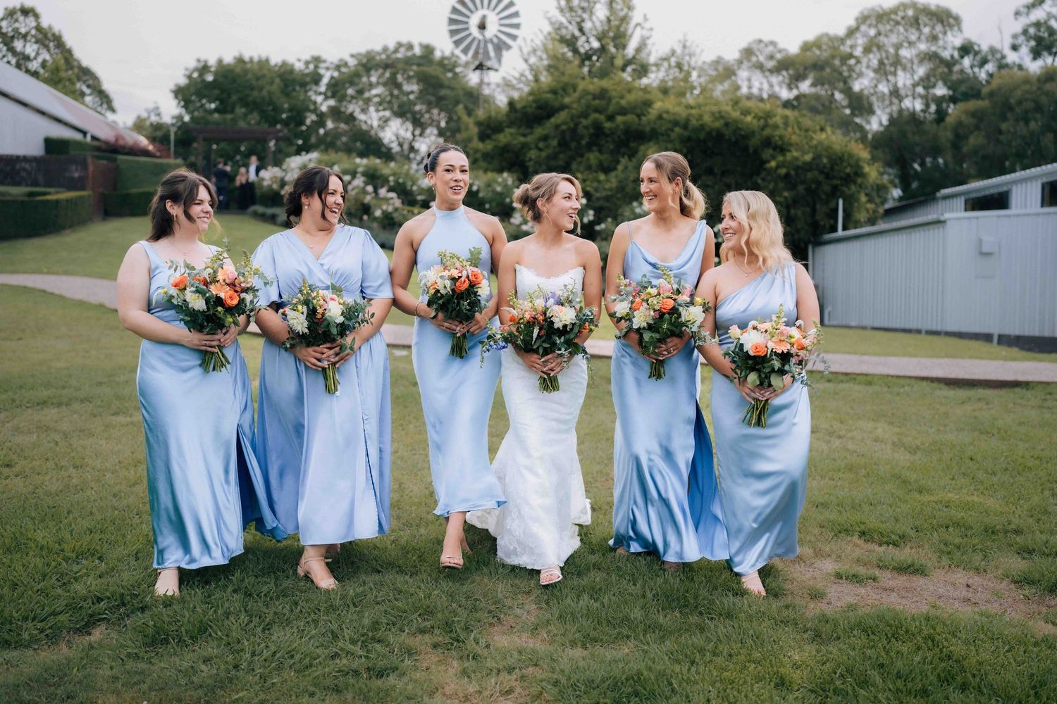 Bride in white gown walking with five bridesmaids in light blue dresses carrying colorful bouquets.