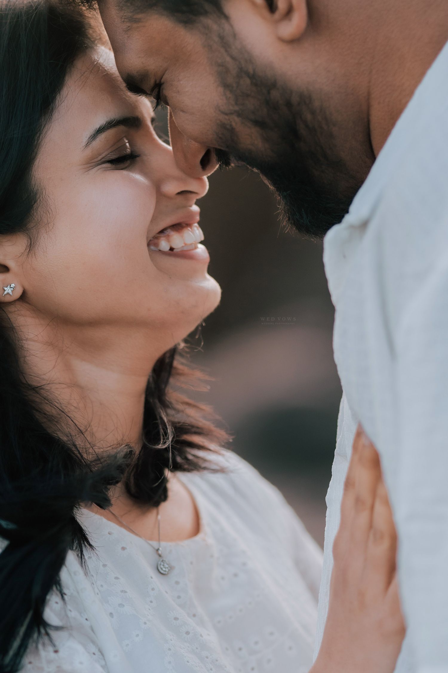 Close-up of smiling woman in white leaning toward bearded man in intimate romantic moment.