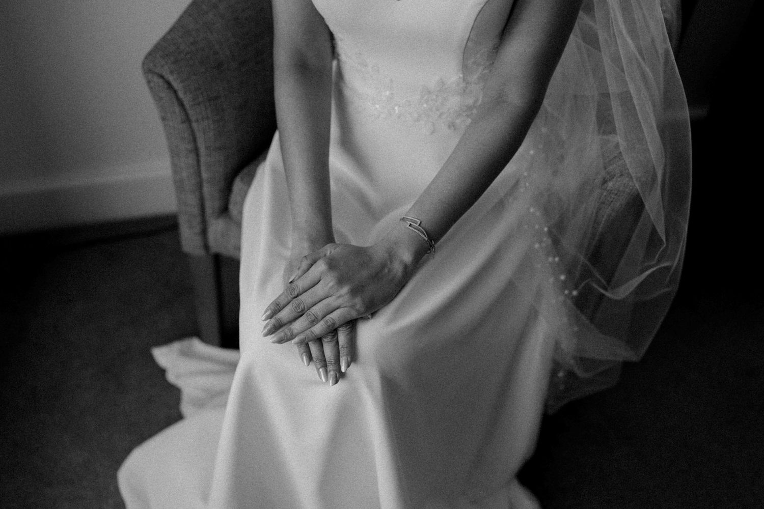 Black and white close-up of bride in wedding gown with delicate lace veil and manicured hands.