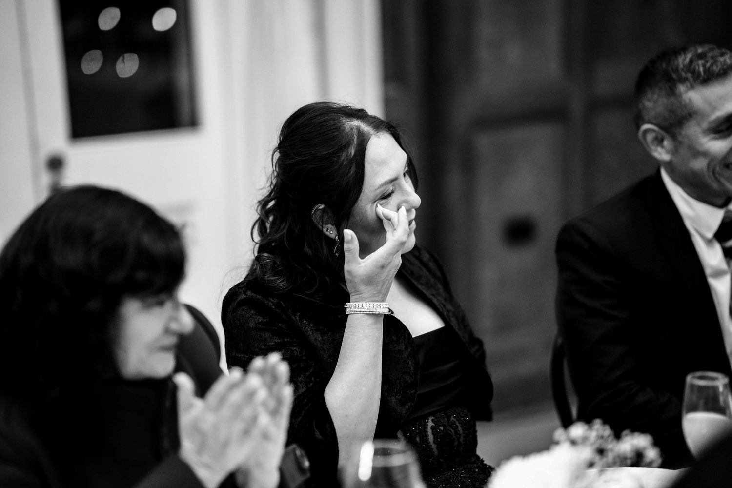 Black and white photo of emotional wedding guest wiping tears at reception dinner table.