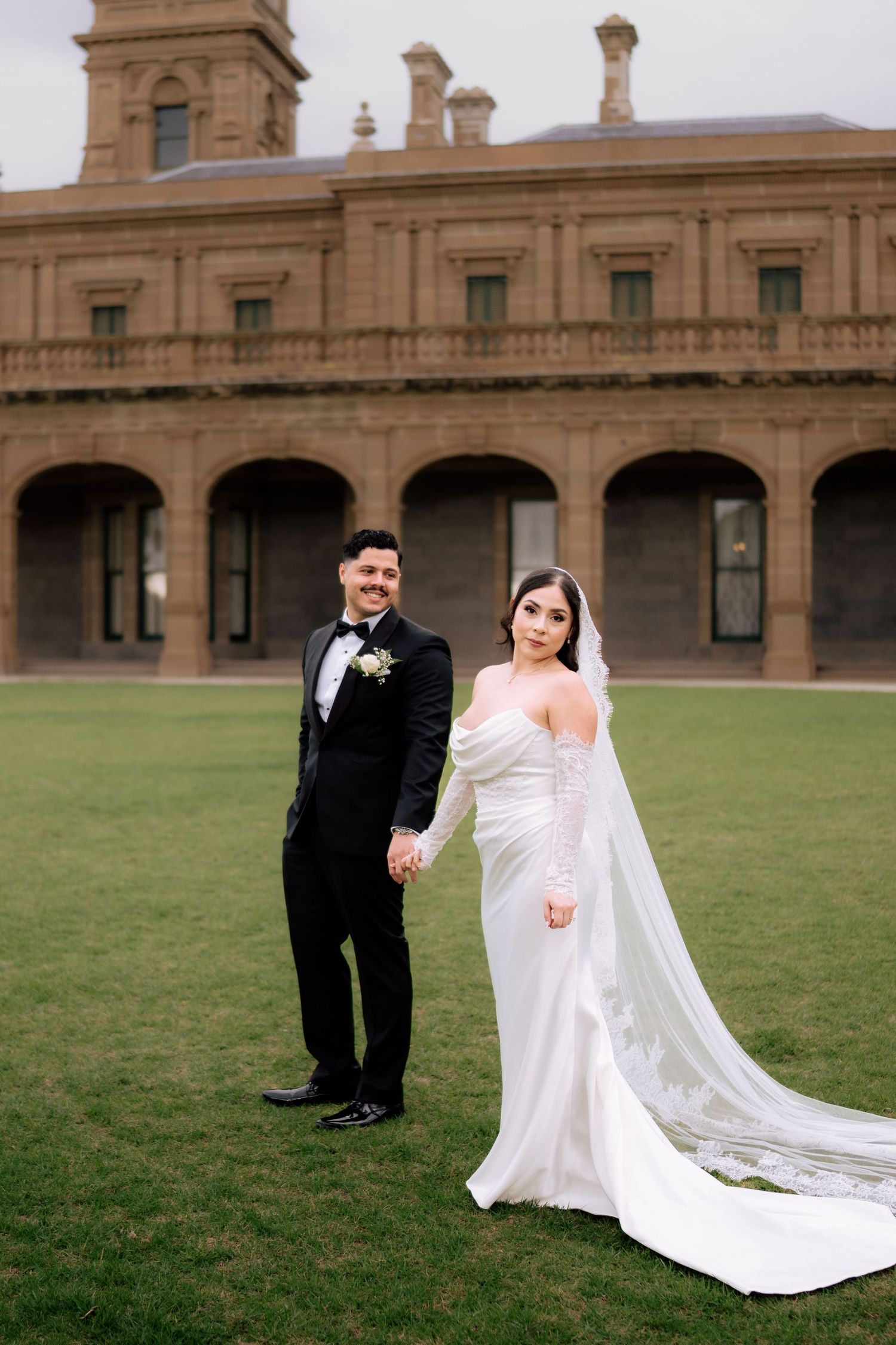 Bride and groom holding hands posing in front of a grand historic building on wedding day.