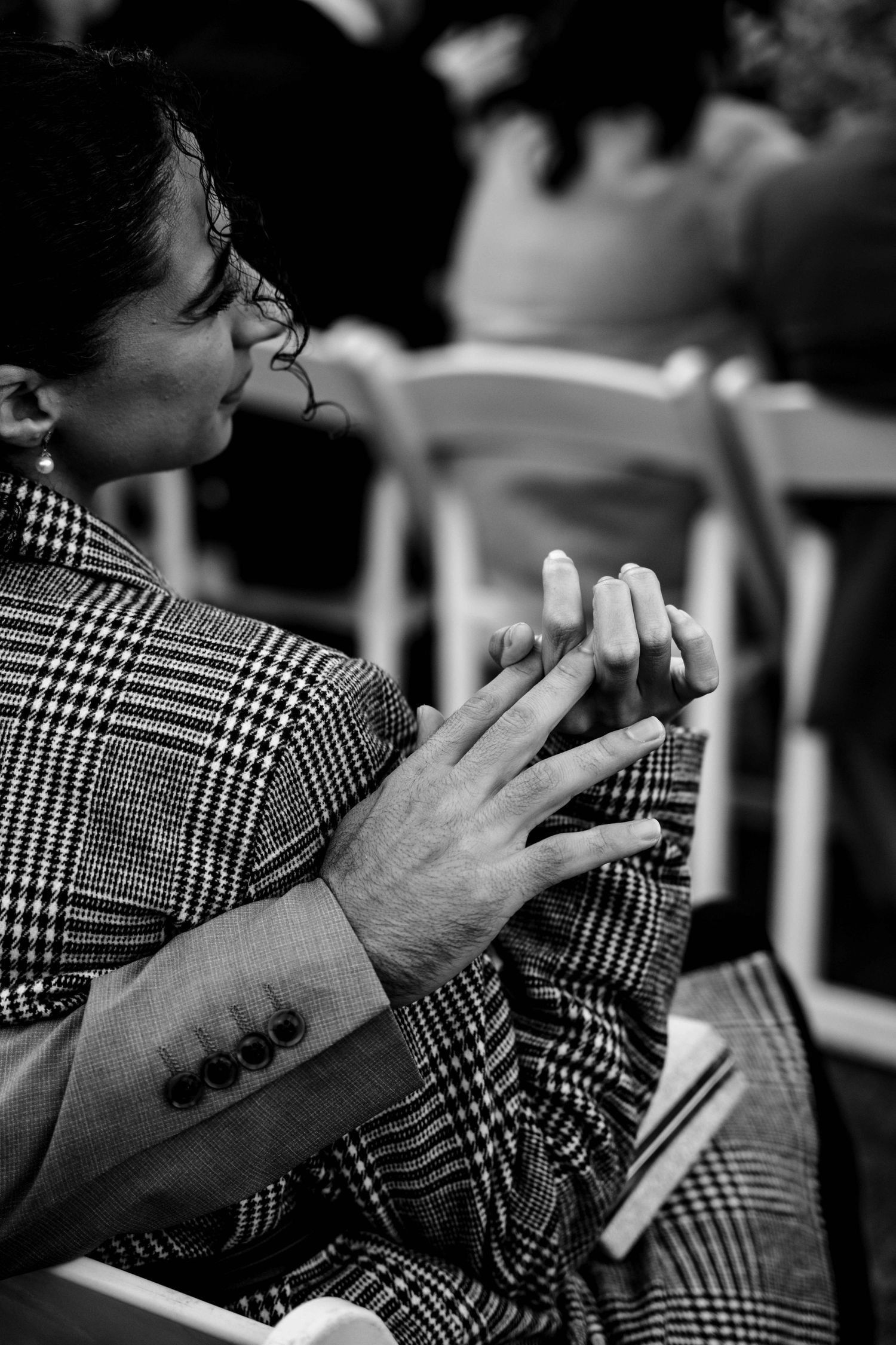 Black and white close-up of wedding guest clasping hands during emotional ceremony moment.
