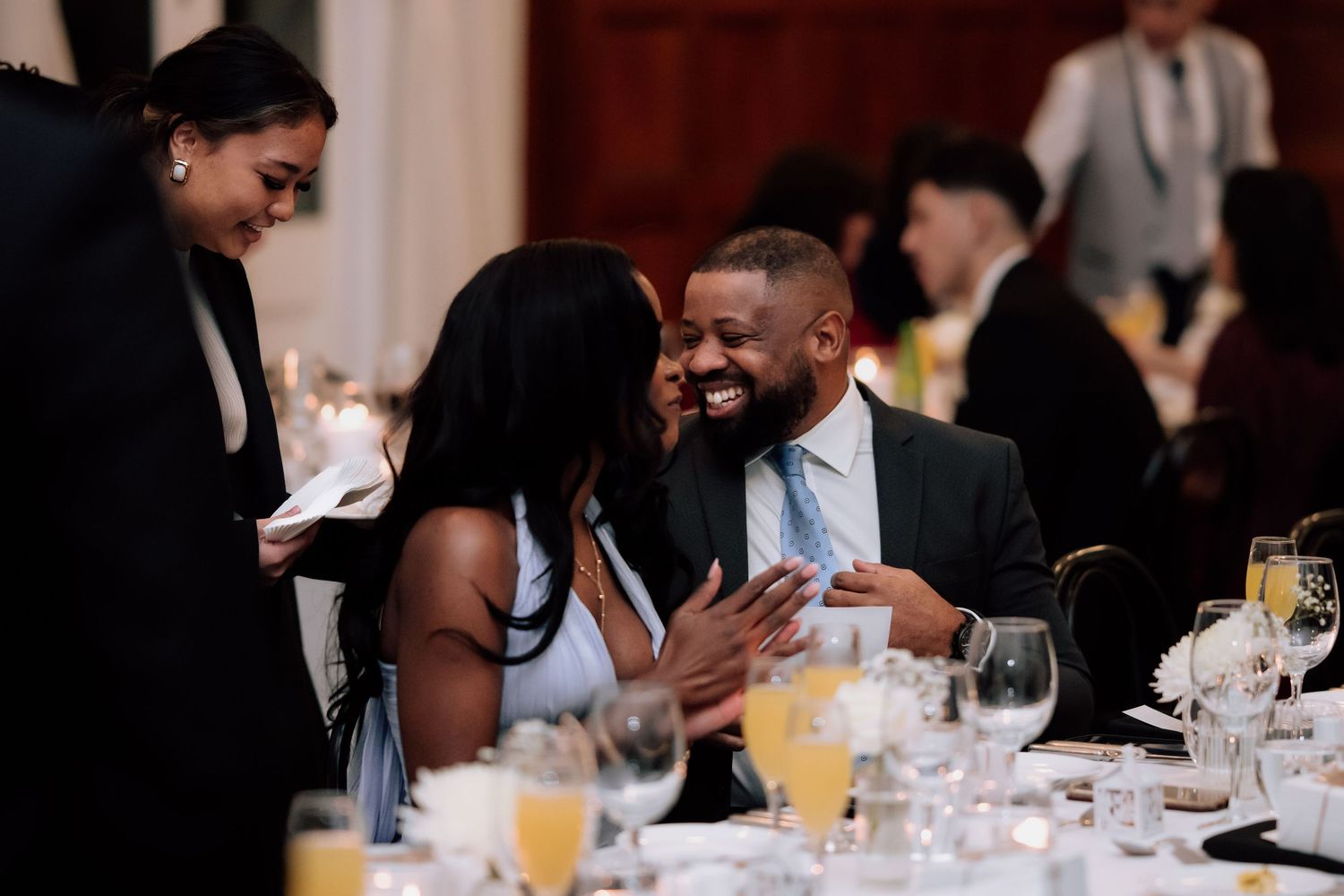 Wedding guests laughing and enjoying conversation at elegantly set reception dinner table.