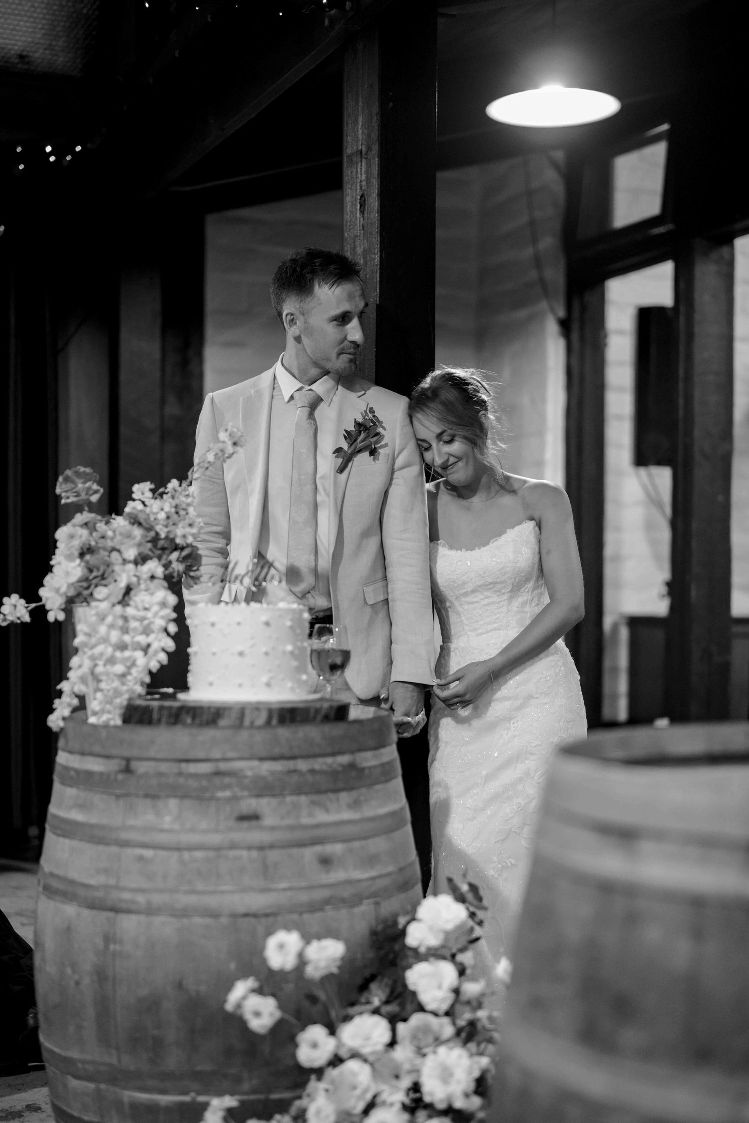 Black and white photo of bride and groom cutting their wedding cake on wooden barrels.