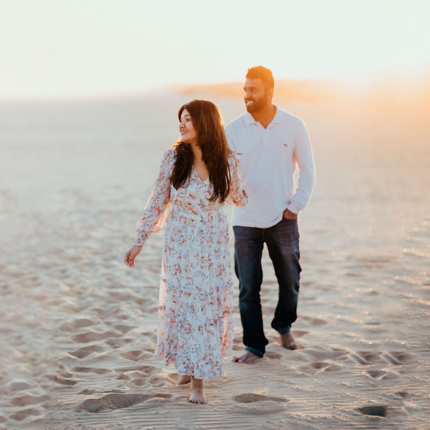 Romantic couple walking on sandy beach at golden sunset in casual elegant attire.