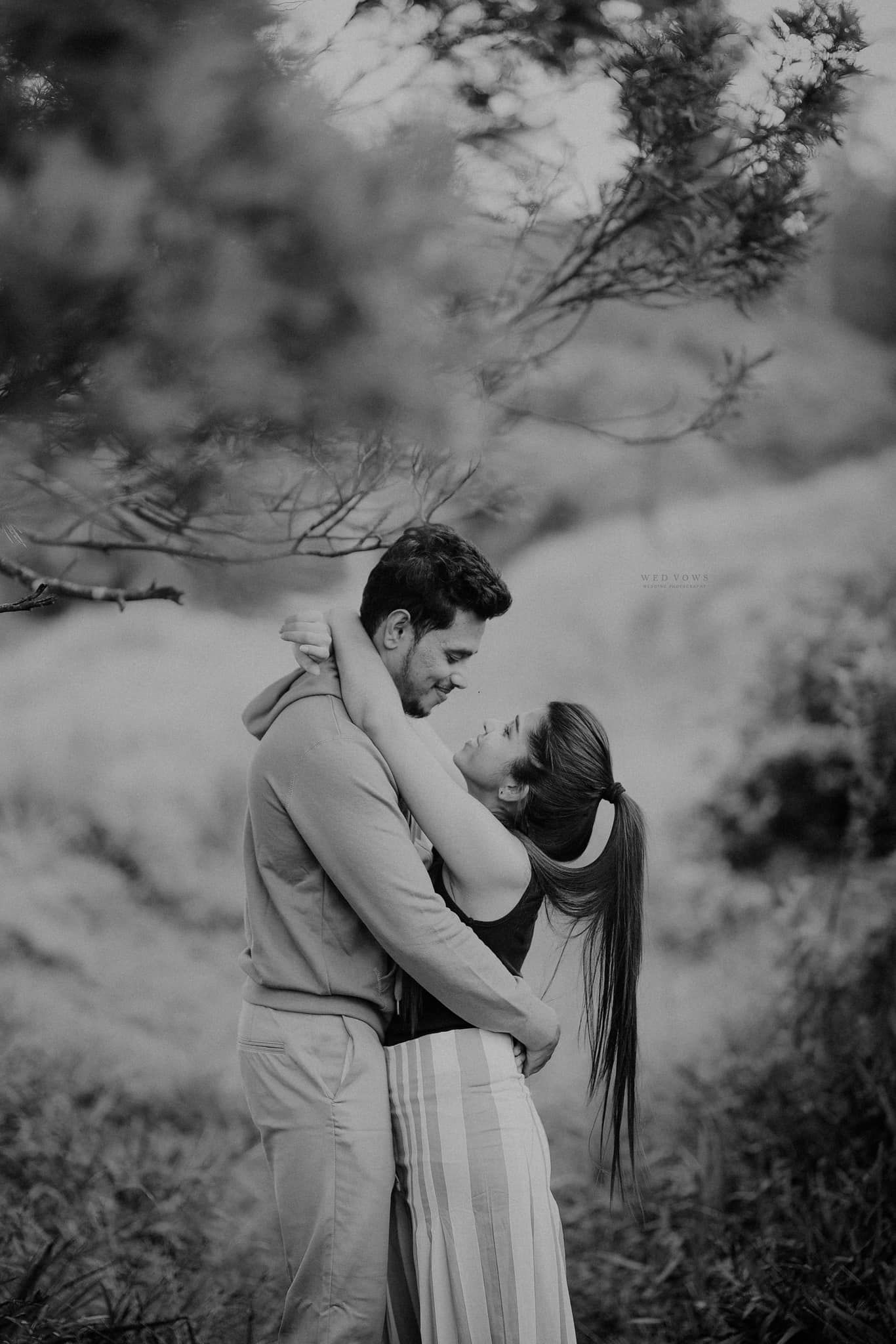 Black and white romantic couple embracing and almost kissing in a natural outdoor forest setting.