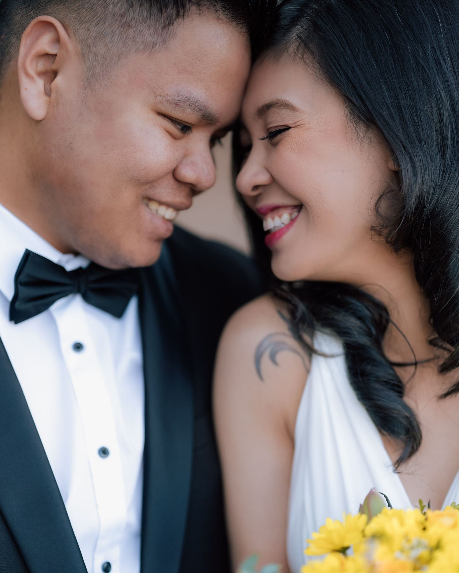 Happy Asian bride and groom in formal wedding attire sharing a joyful close moment.