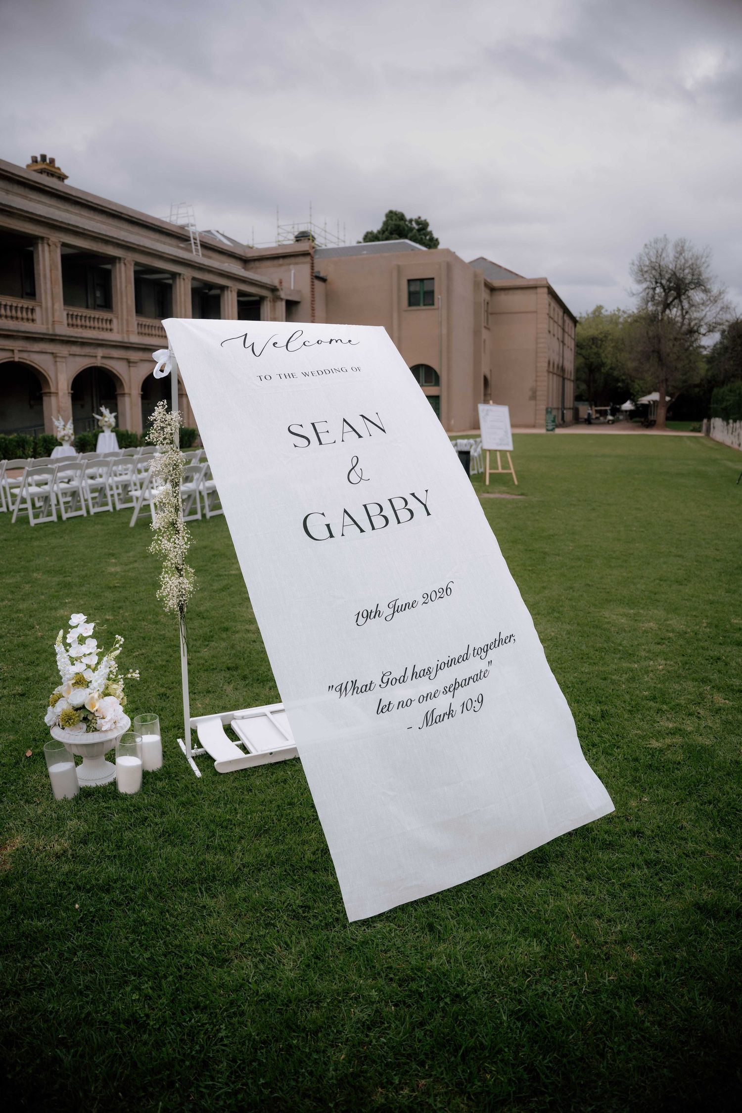 Elegant outdoor wedding welcome sign for Sean and Gabby on green lawn with white chairs and floral arrangements.
