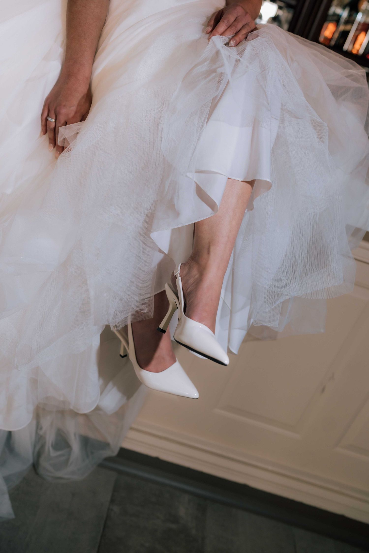 Close-up of bride wearing white pointed-toe heeled wedding shoes beneath a layered tulle gown.