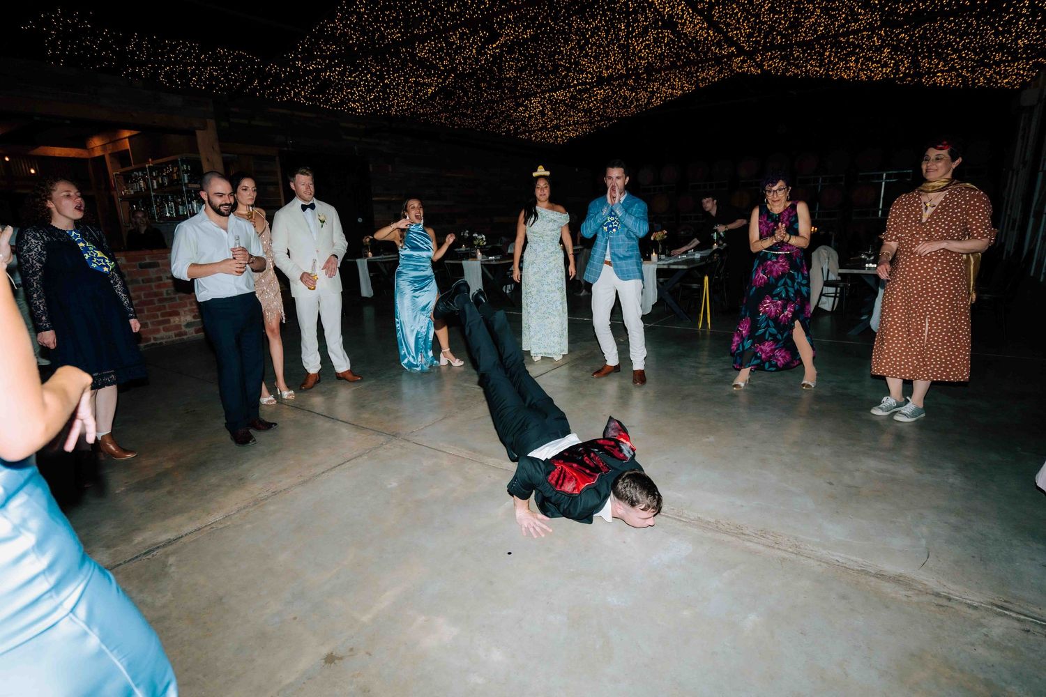 Breakdancer performing headspin at wedding reception while guests watch and cheer in decorated venue.