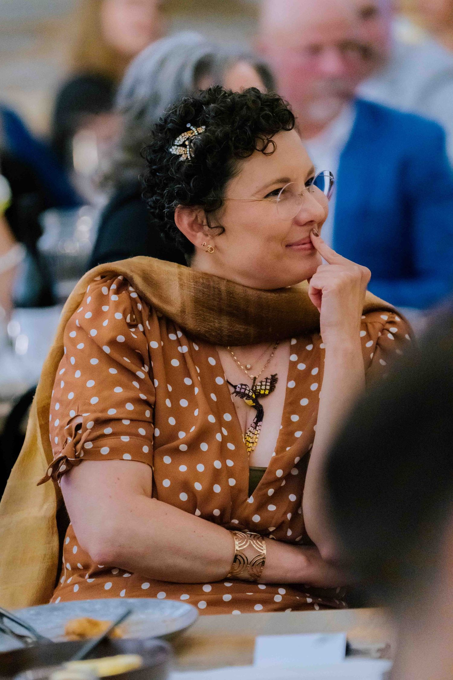 Elegant woman in polka dot dress smiling thoughtfully at a wedding reception.