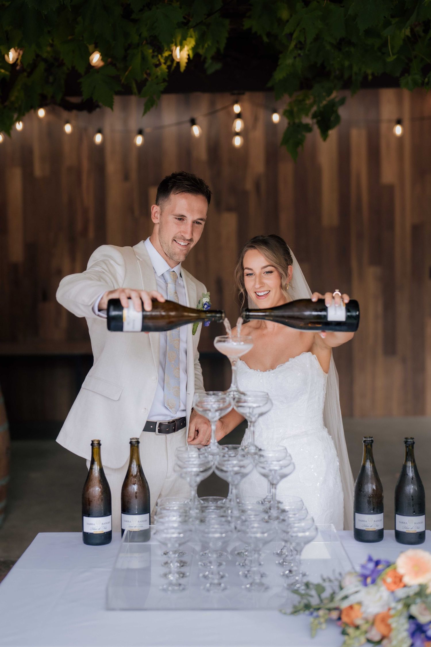 Bride and groom smiling while pouring champagne tower at wedding reception.
