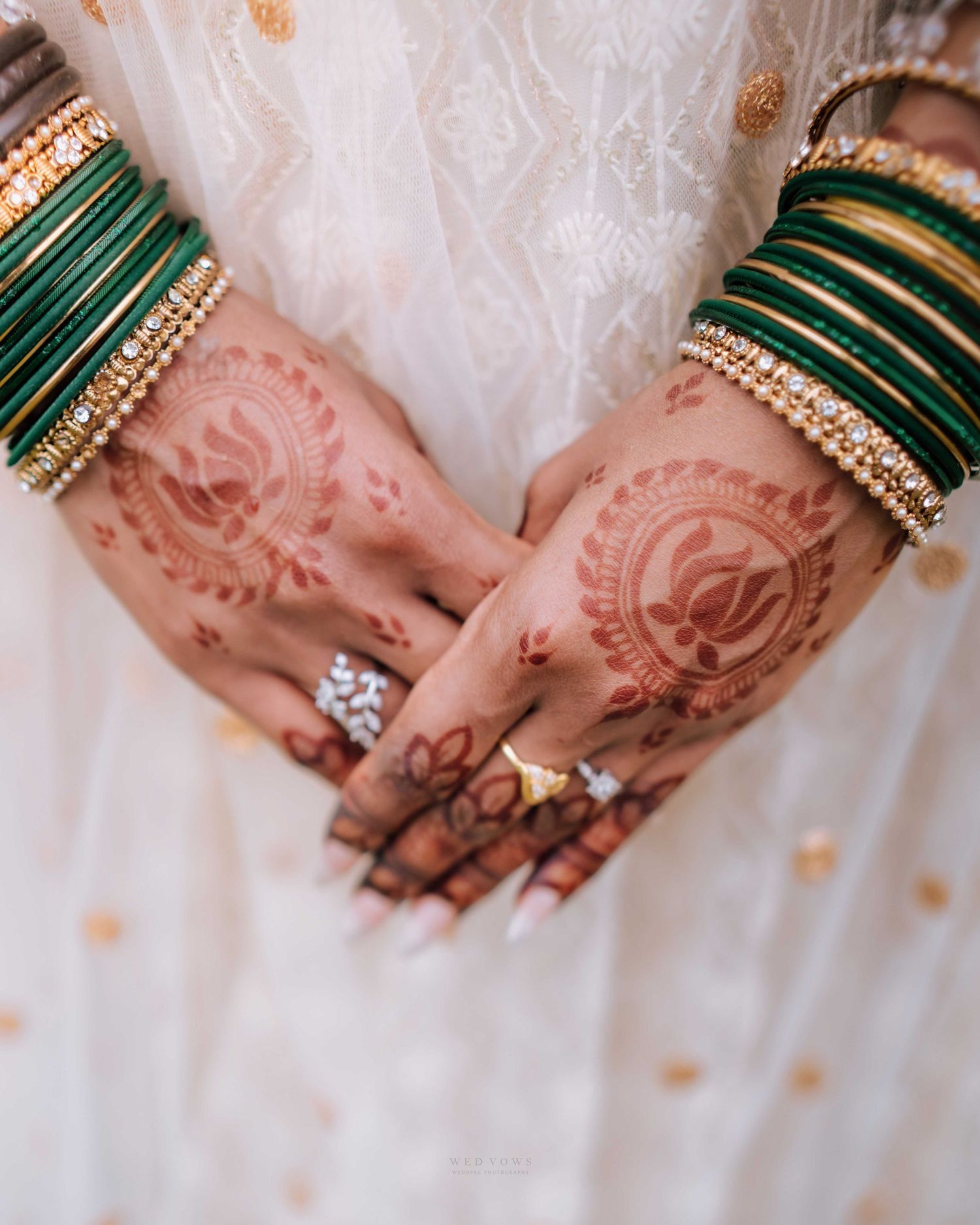 Close-up of Indian bride's hands adorned with intricate mehndi henna and green gold bangles.