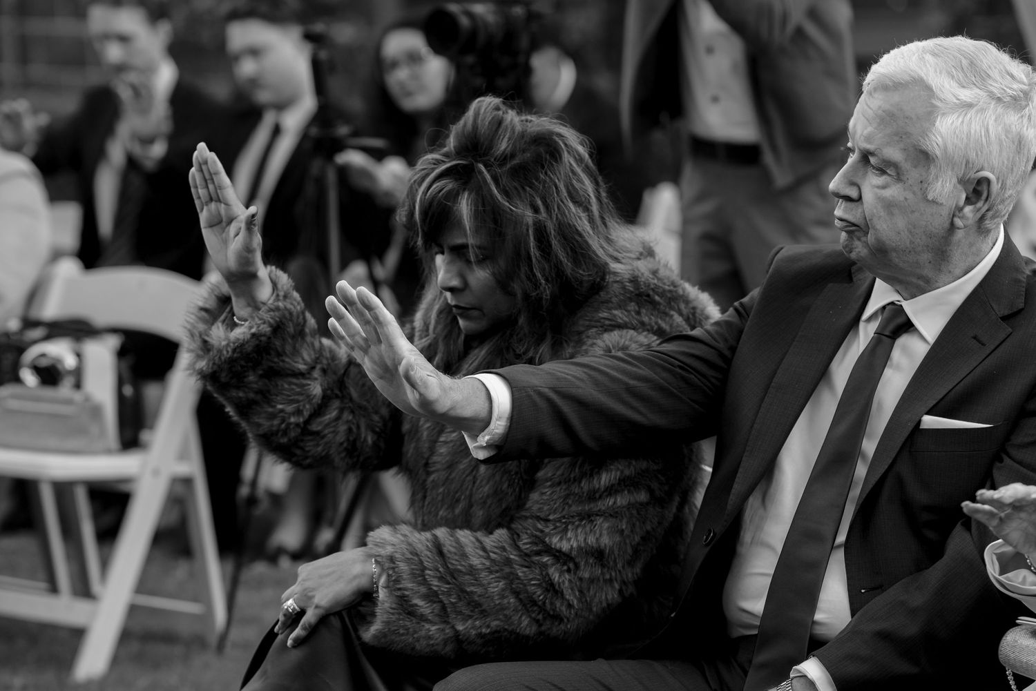 Black and white photo of emotional wedding guest gesturing with hands while seated beside older man.