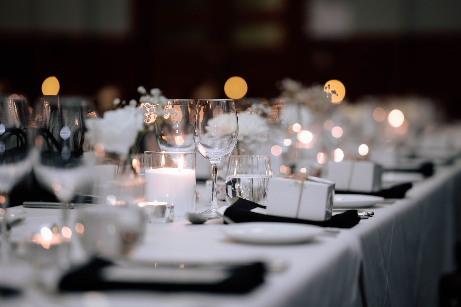 Elegant wedding reception table set with white linens, candles, glassware, and soft bokeh lighting.
