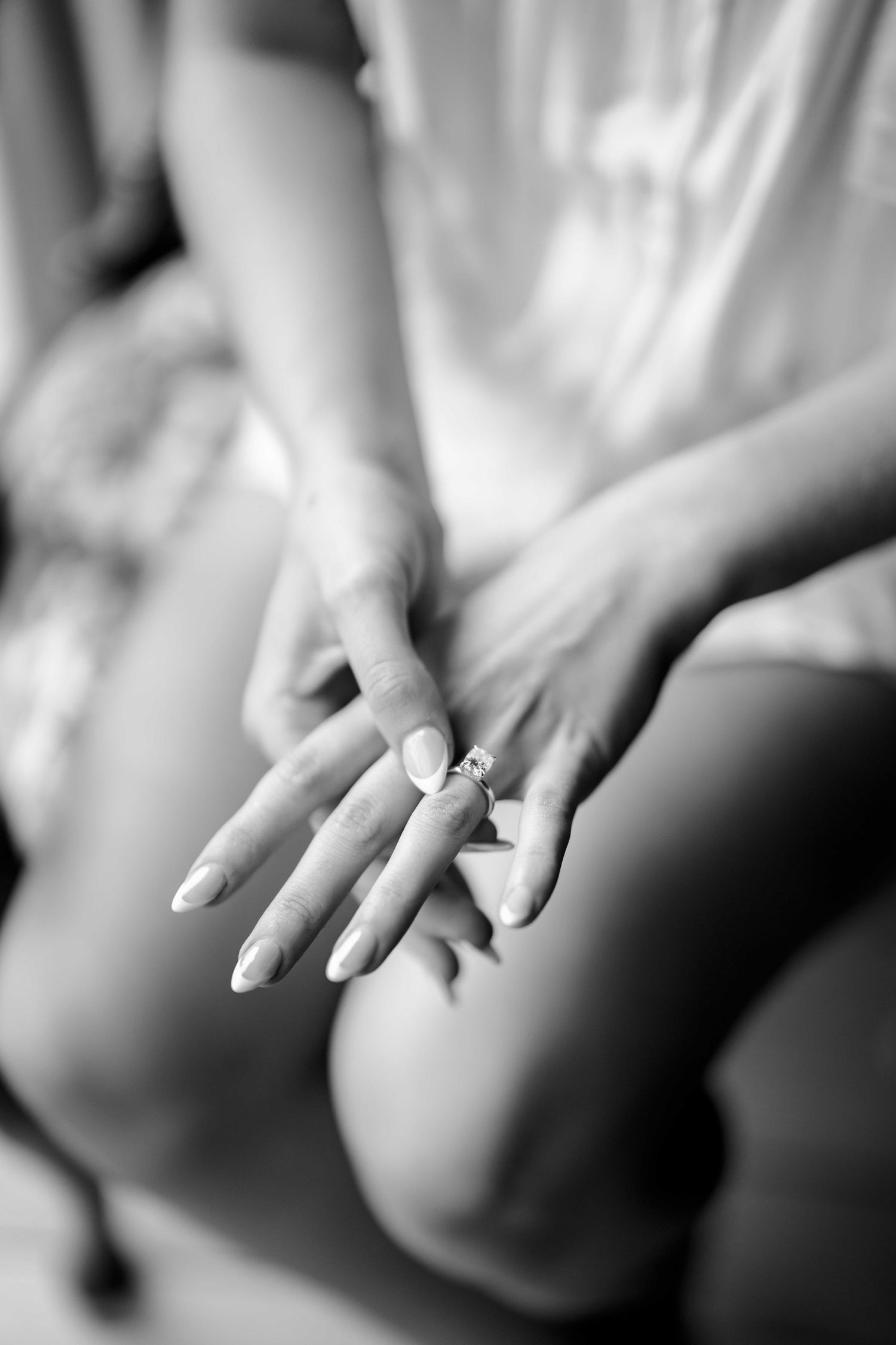Black and white close-up of bride's hands displaying sparkling diamond engagement ring.