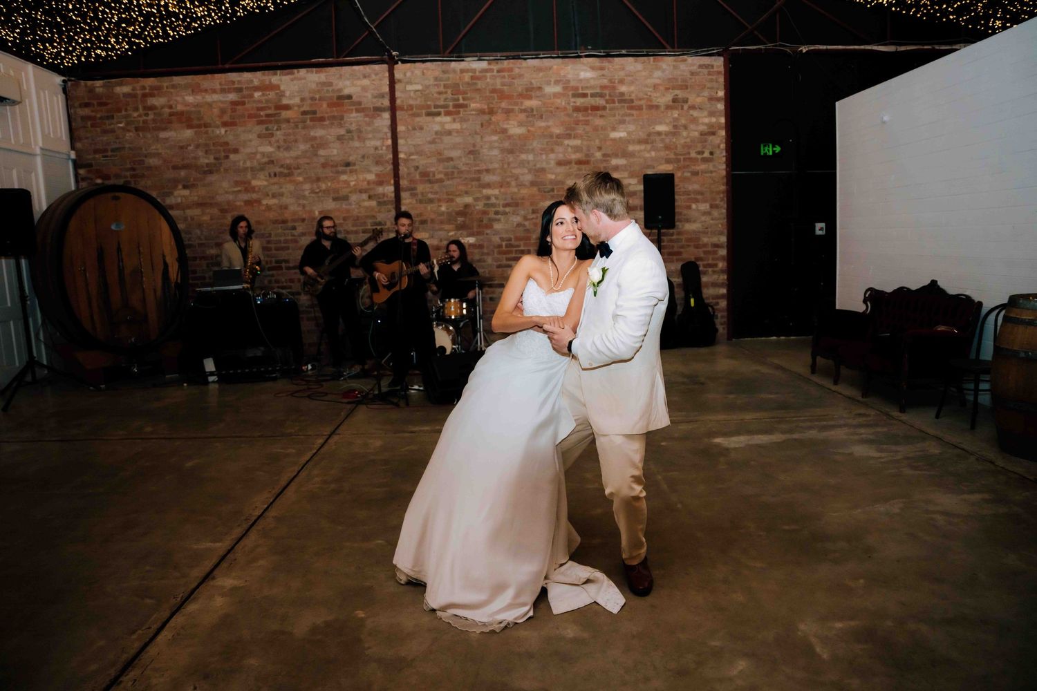 Bride and groom sharing an intimate first dance in a rustic venue with live band performing.