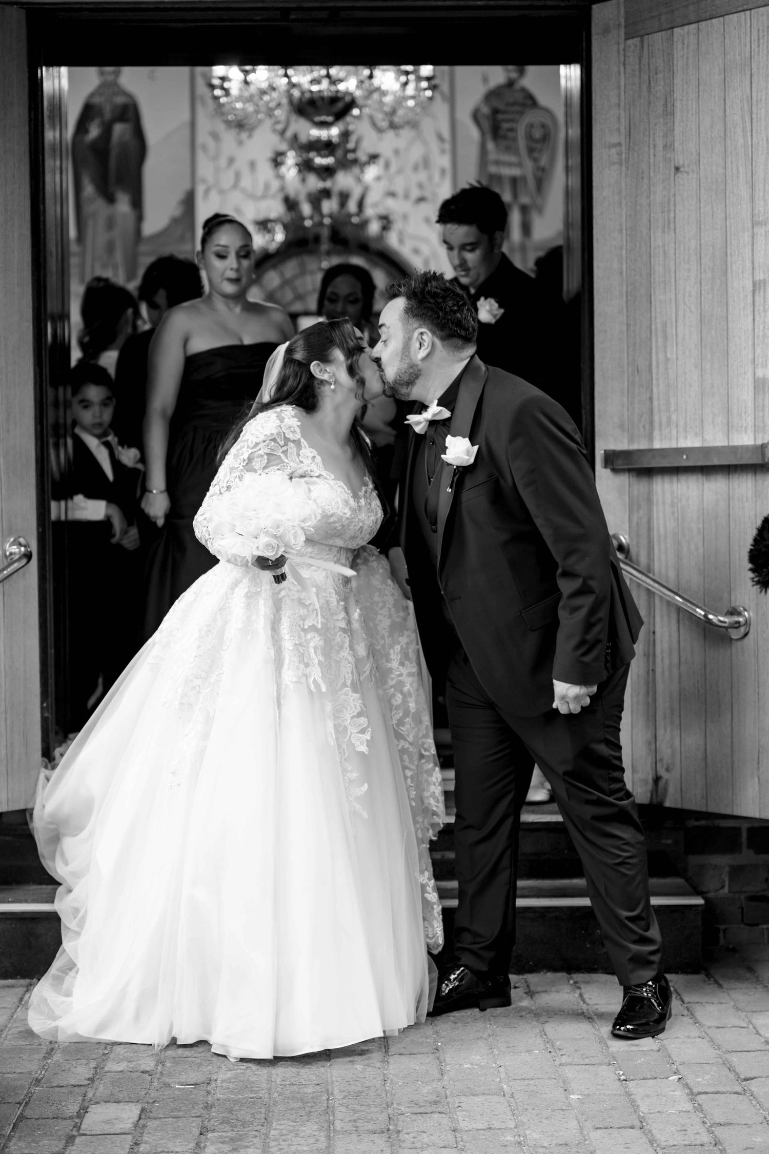 Bride and groom sharing a kiss at the church entrance after their wedding ceremony in black and white.