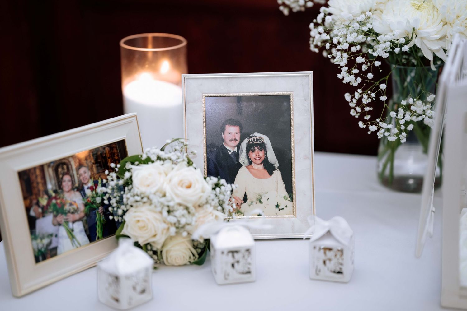 Wedding memory table with framed photos, white roses, baby's breath, and glowing candles.