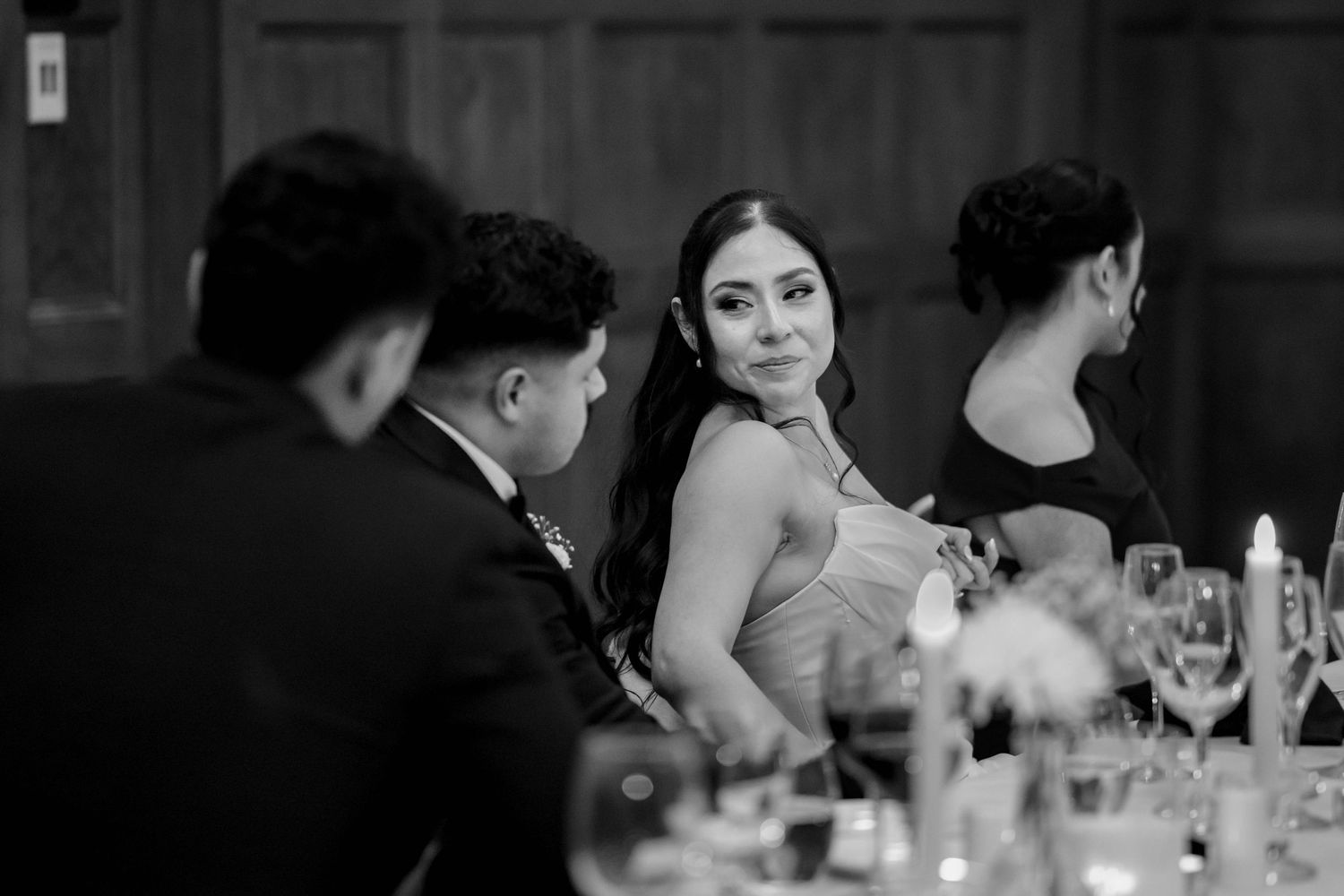 Black and white photo of elegant wedding guest glancing sideways at reception dinner table.