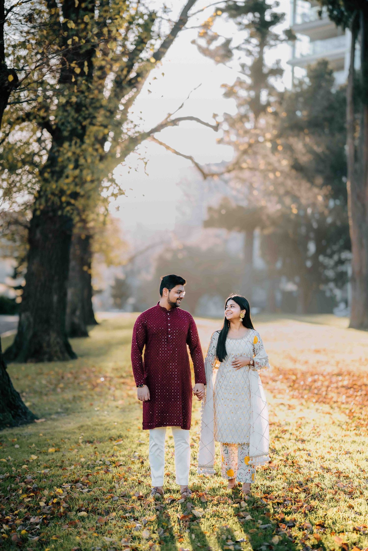 Couple in traditional Indian outfits walking hand in hand through a misty autumn park.