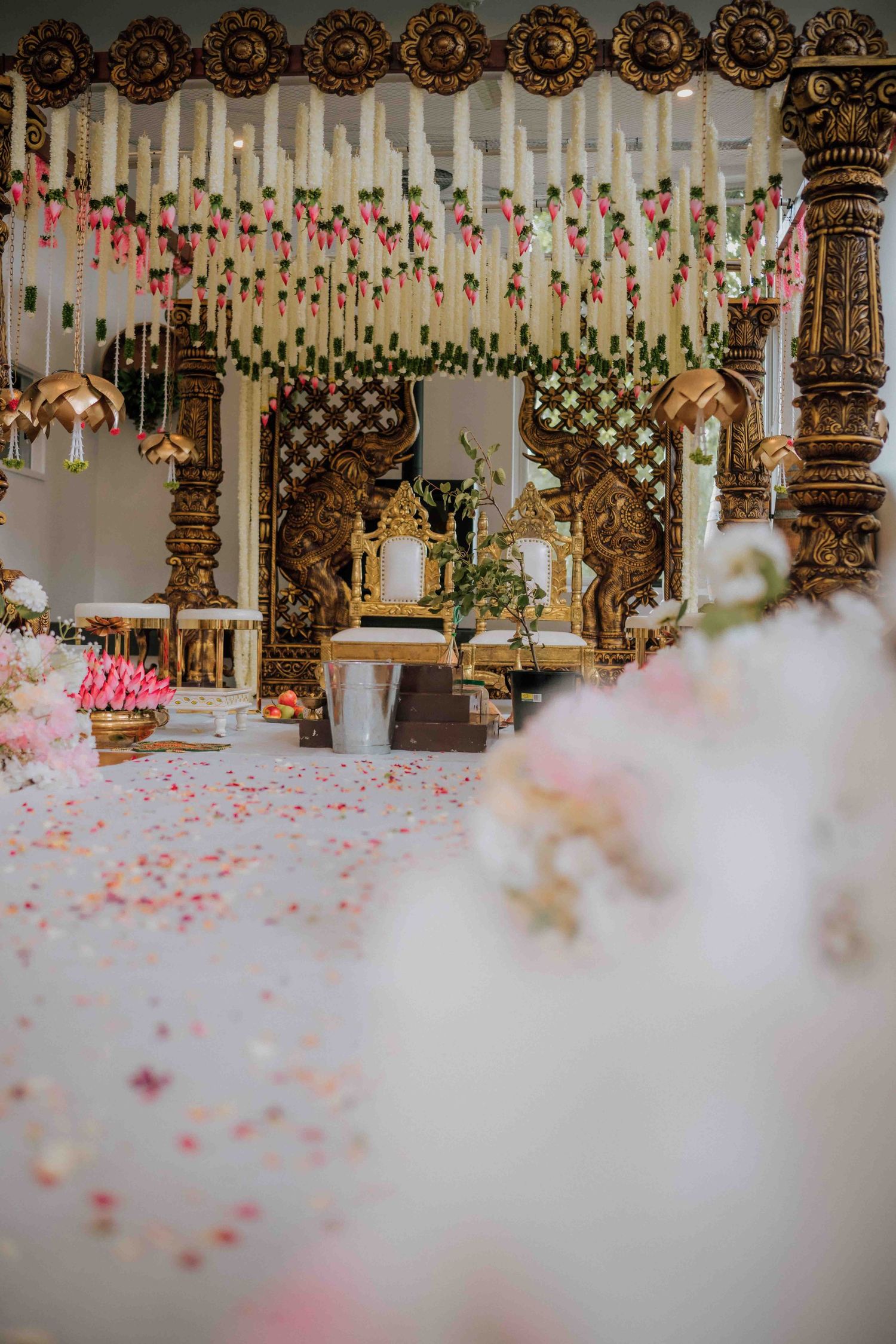 Elegant empty Hindu wedding mandap with ornate golden pillars and hanging pink floral decorations.