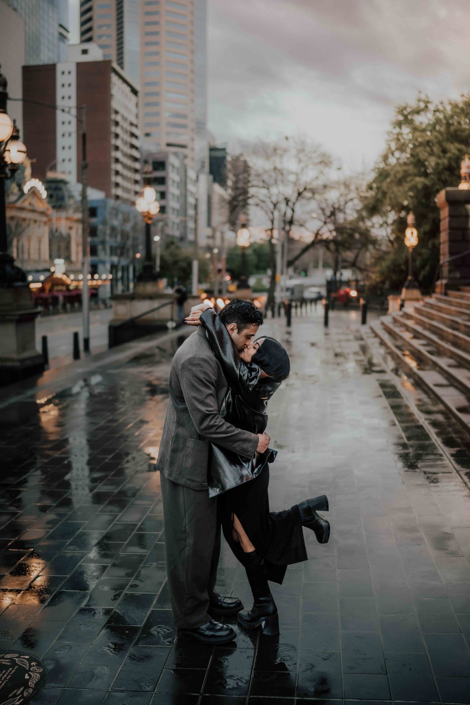 Couple sharing a passionate embrace and kiss on a rainy city street at dusk.