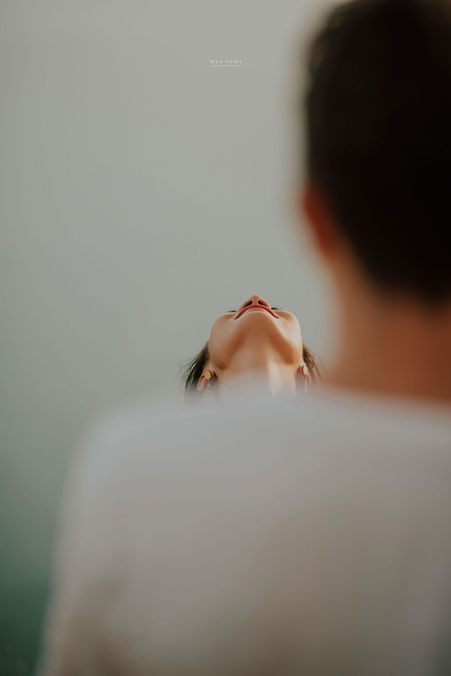 A tender close-up of a woman leaning back with eyes closed, framed by a mans shoulder in white shirt.