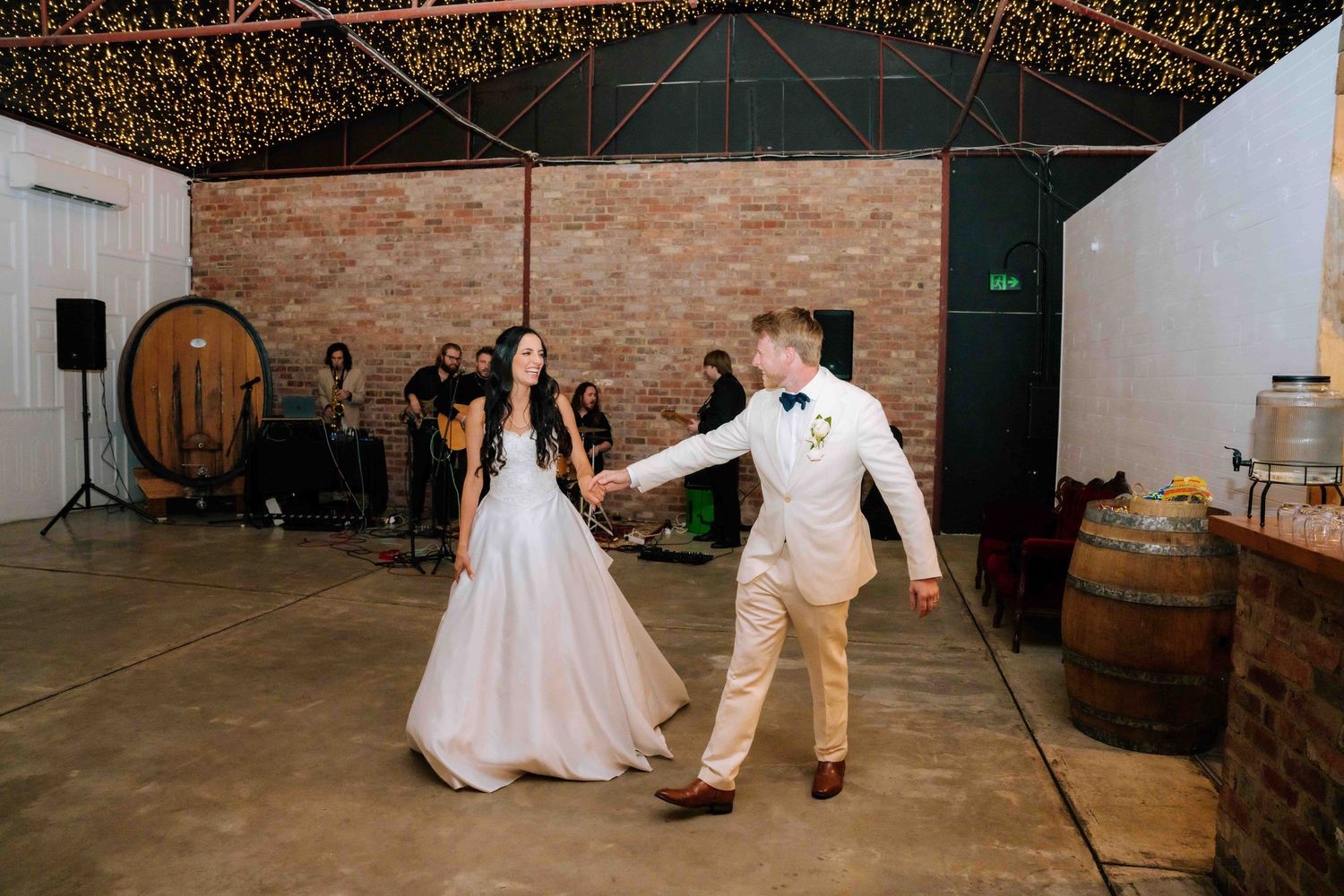 Bride and groom sharing first dance in rustic barn venue decorated with fairy lights.