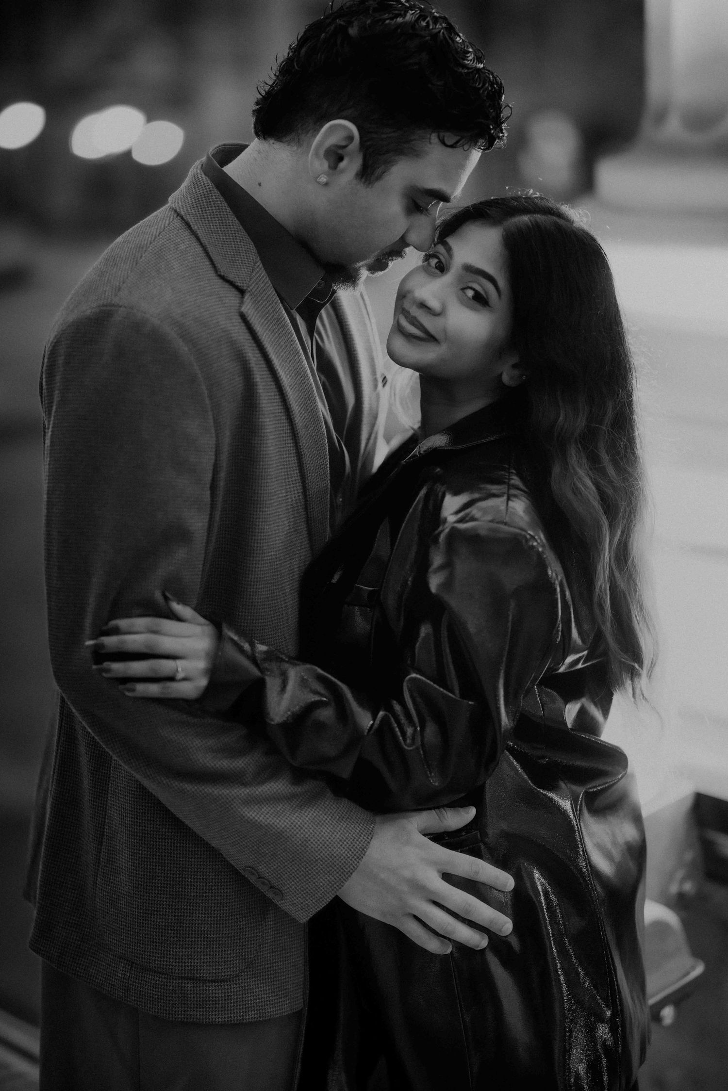 Black and white romantic portrait of a couple embracing tenderly in a city at night.