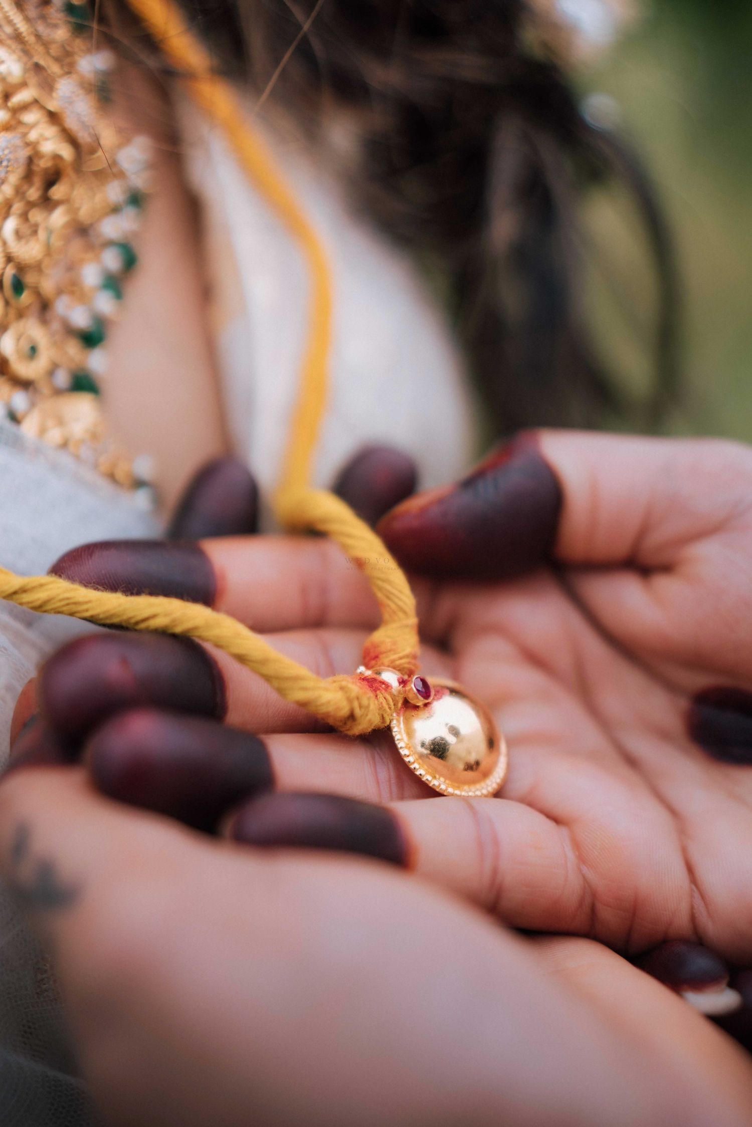 Close-up of Indian bride holding gold mangalsutra pendant on yellow thread with henna-adorned hands.