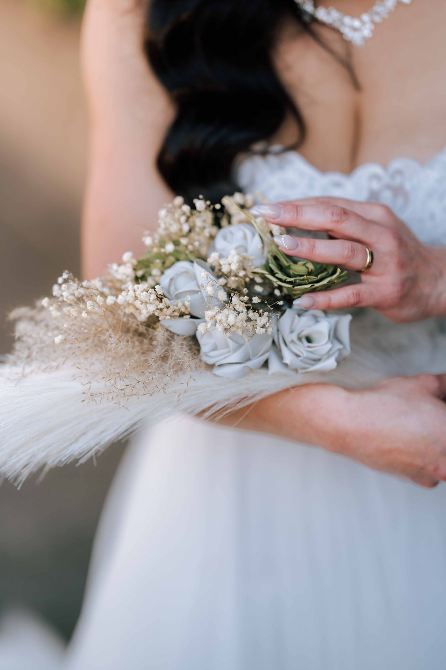 Close-up of a bride holding a boho wedding bouquet with white roses and pampas grass.