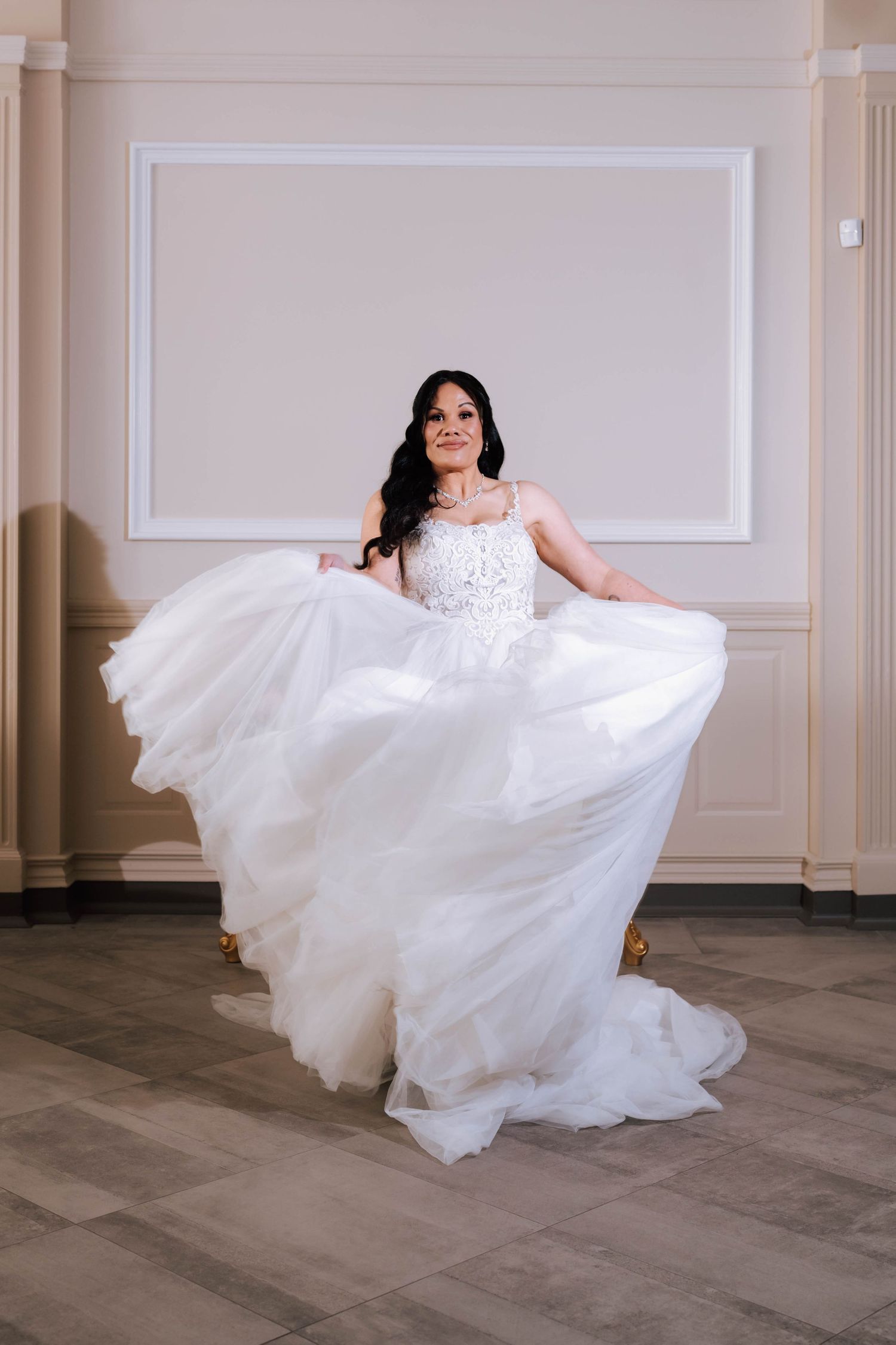 Bride in a flowing white tulle ball gown twirling gracefully in an elegant white-walled venue.
