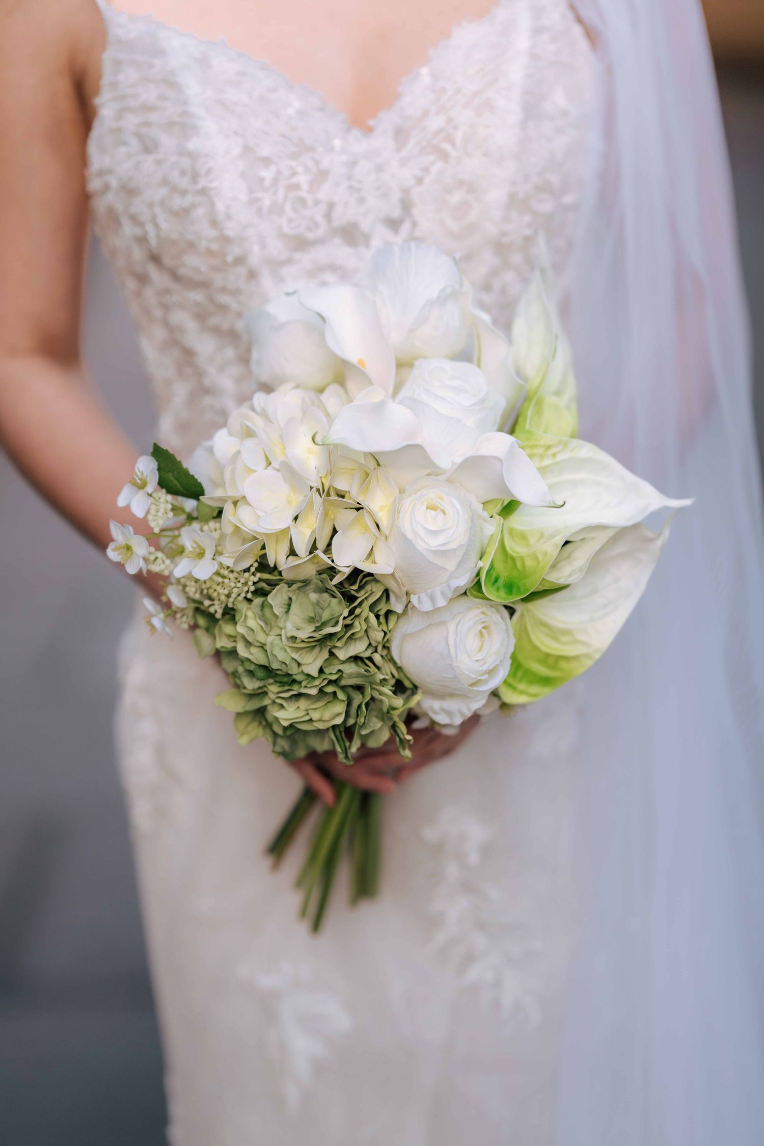 Close-up of bridal bouquet featuring white roses, hydrangeas, and green accents held by bride.