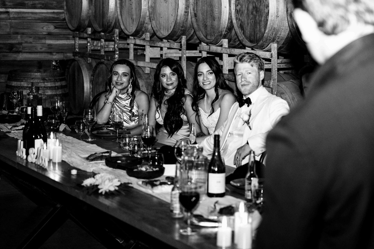 Black and white photo of guests socializing at a winery bar surrounded by oak barrels.