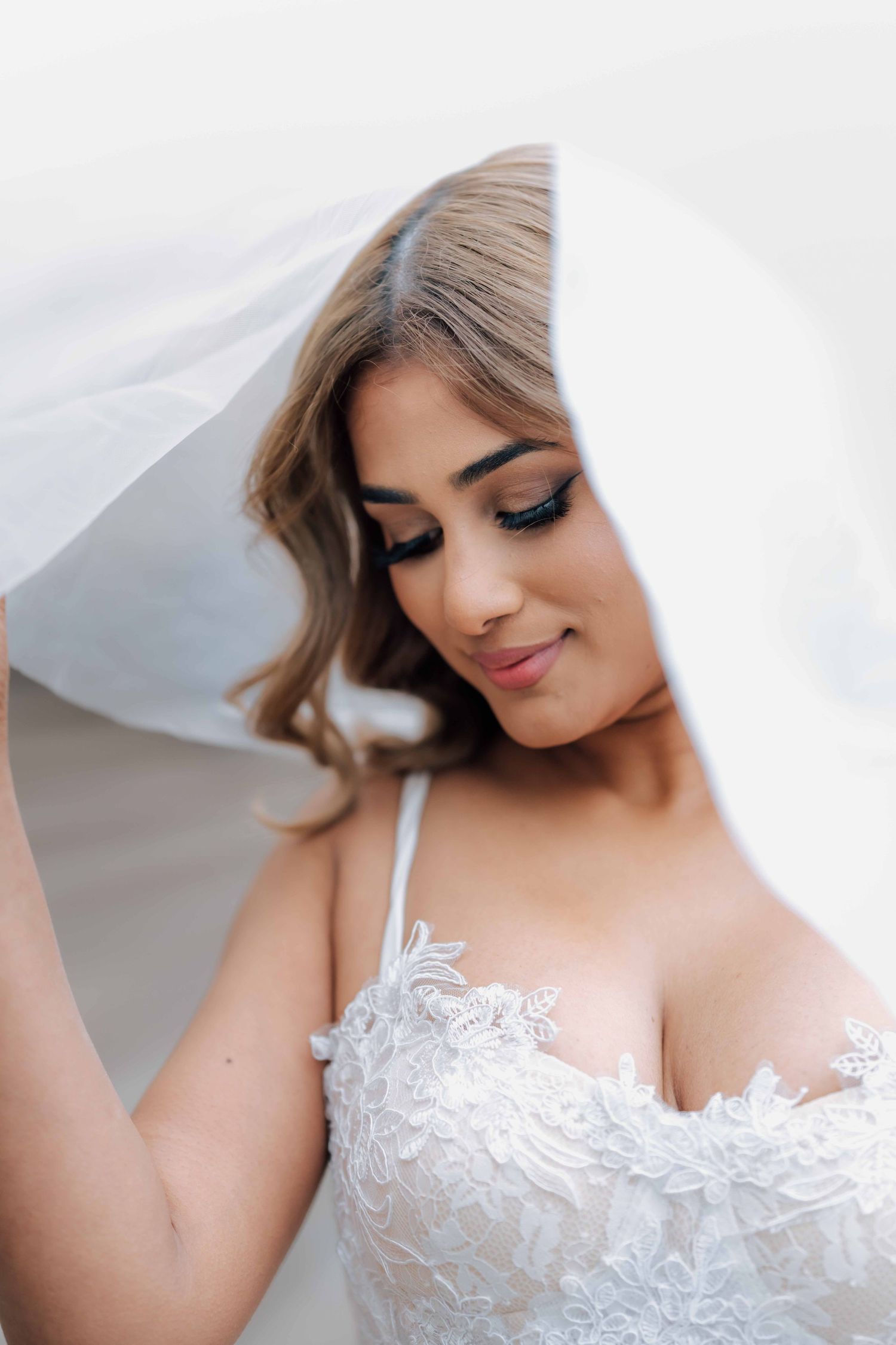 Beautiful bride smiling softly under flowing white veil wearing lace bodice wedding dress.