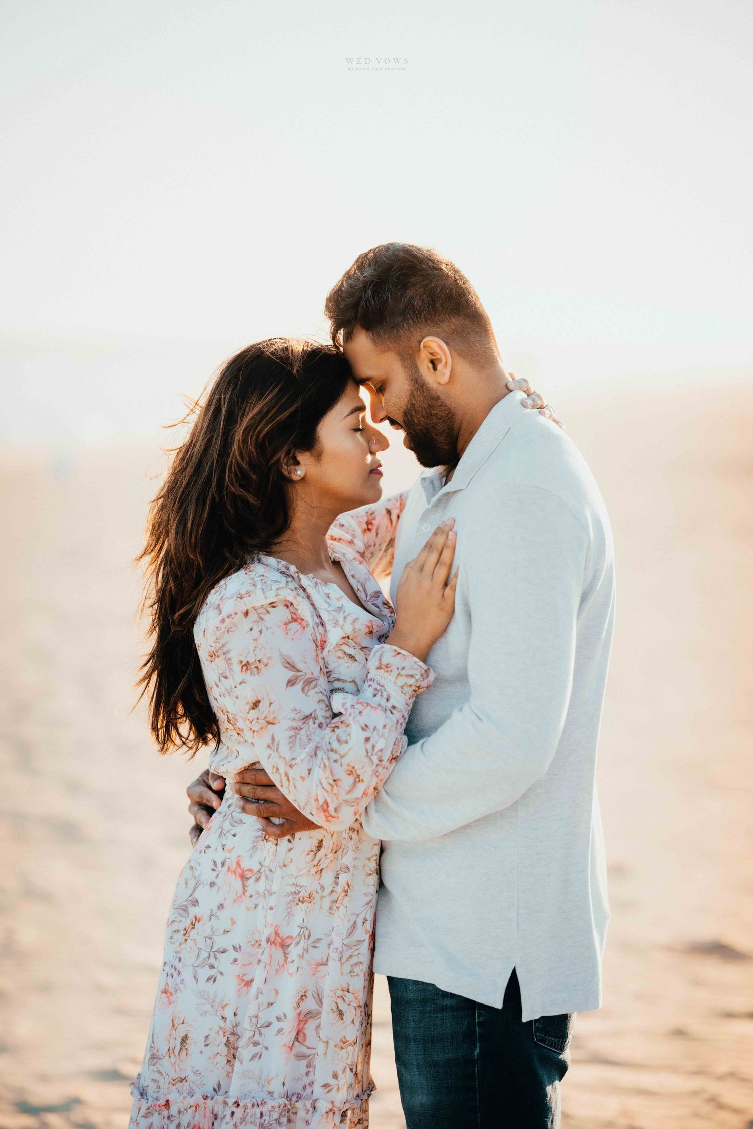 Romantic couple embracing face to face on a sandy beach during a warm golden sunset.