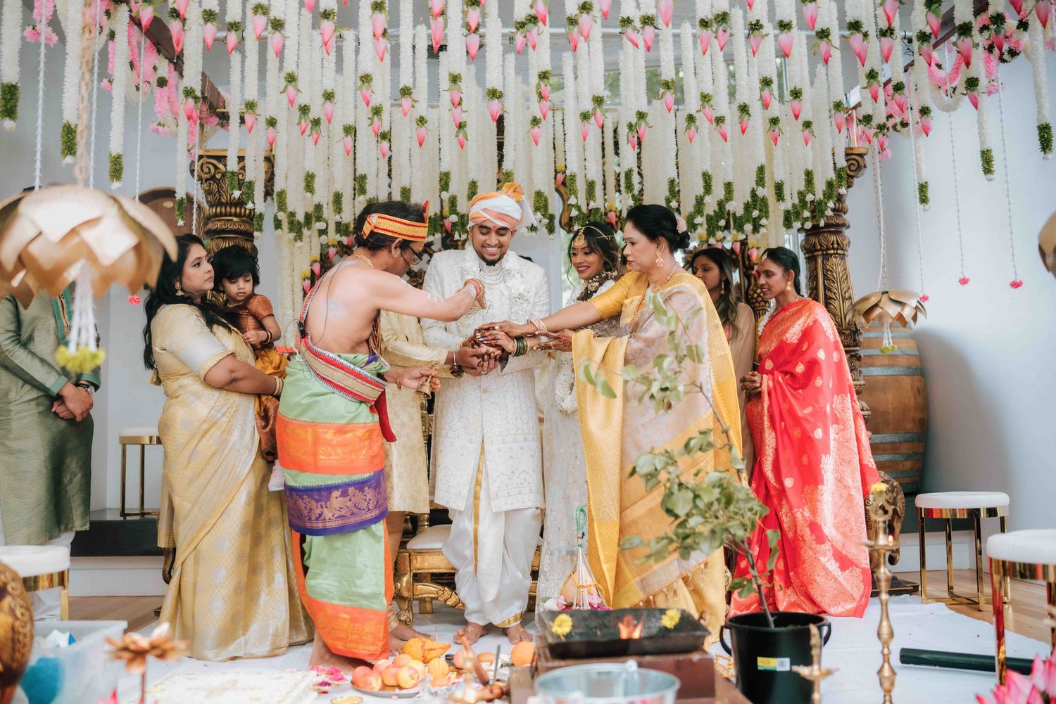 Family members join hands during a traditional Hindu wedding ceremony under floral decorations.