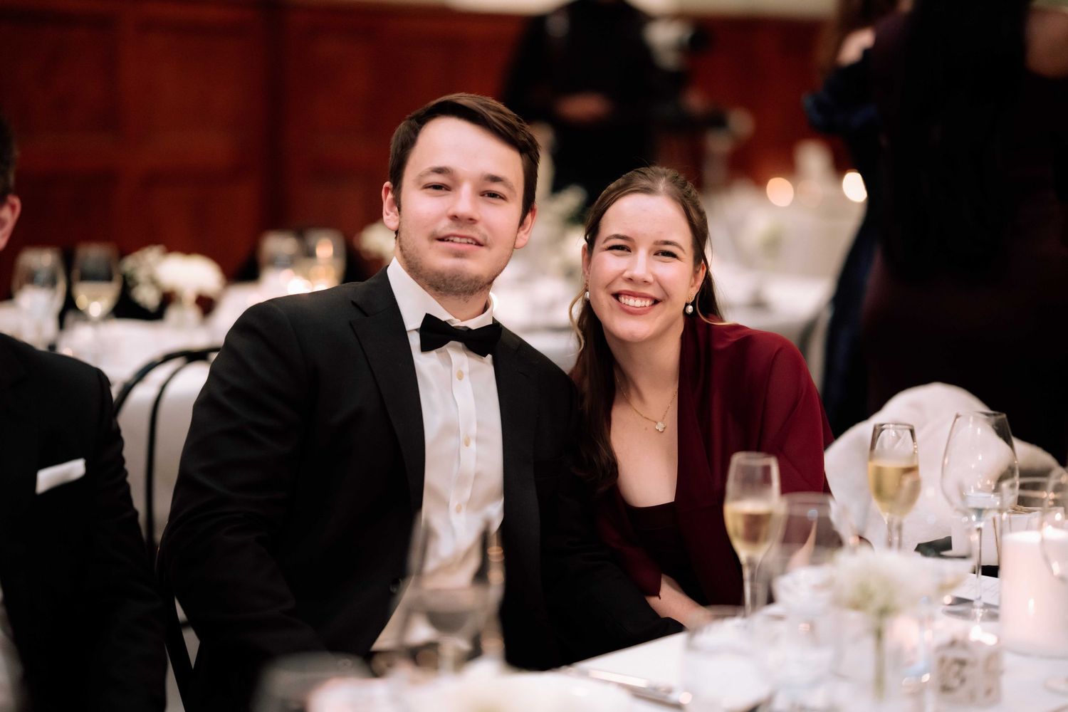 Smiling couple in formal attire seated together at an elegant wedding reception dinner table.