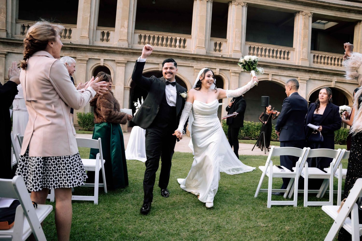 Joyful newlyweds celebrate recessional walk down the aisle at outdoor wedding ceremony with guests.