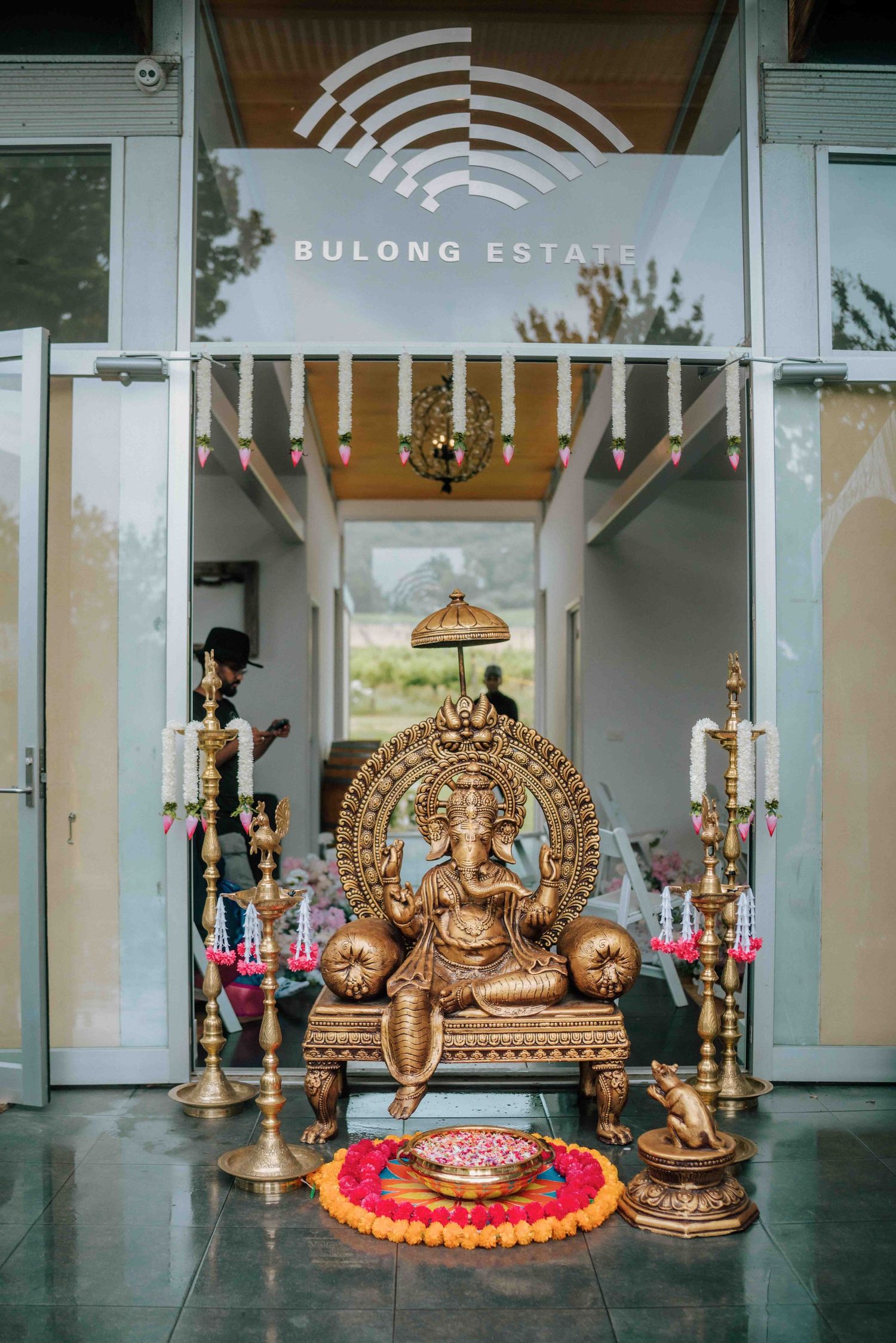 Golden Ganesha statue with brass lamps at Bulong Estate entrance decorated for a Hindu wedding.