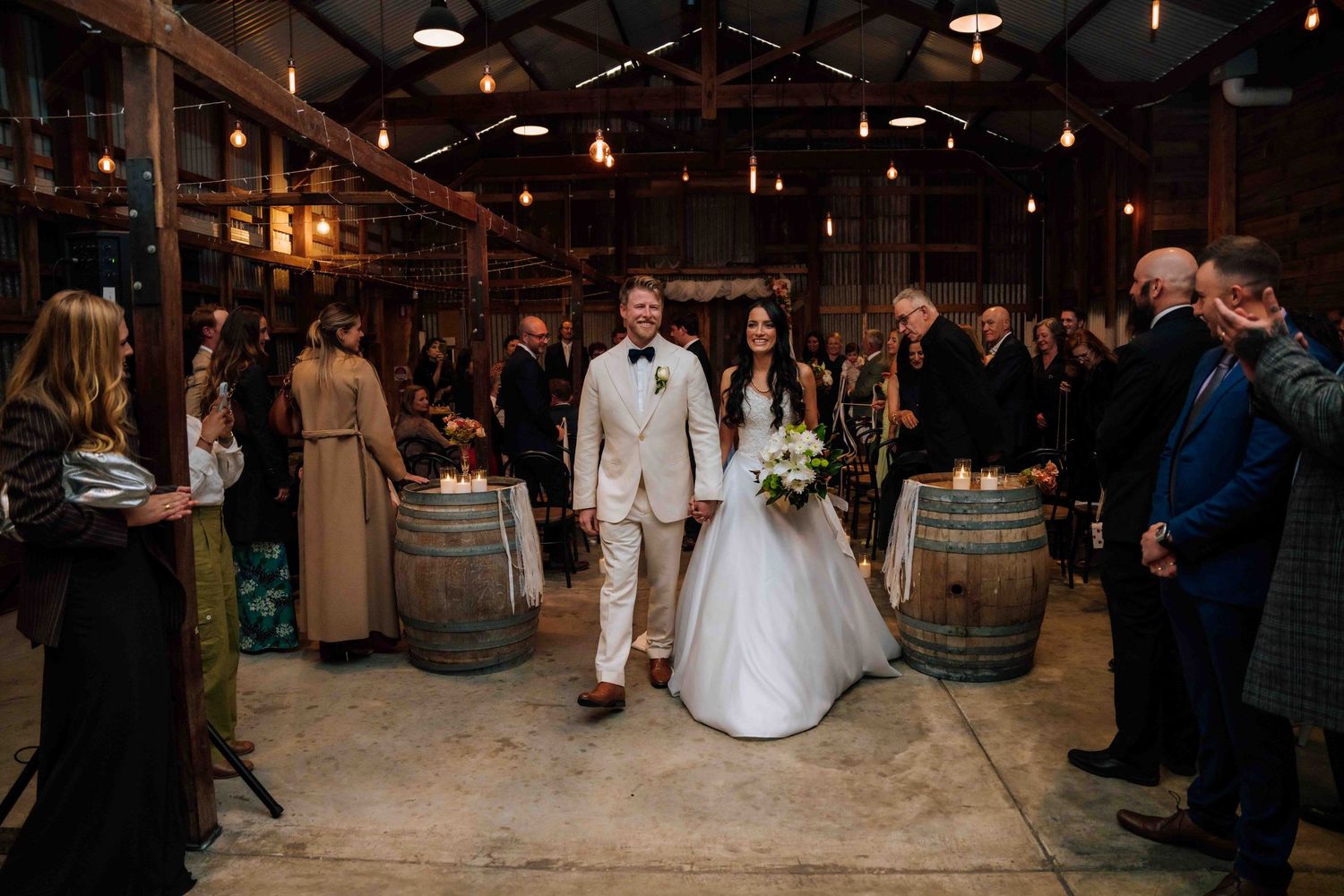 Bride and groom walking down the aisle in a rustic barn wedding venue with barrel decorations.