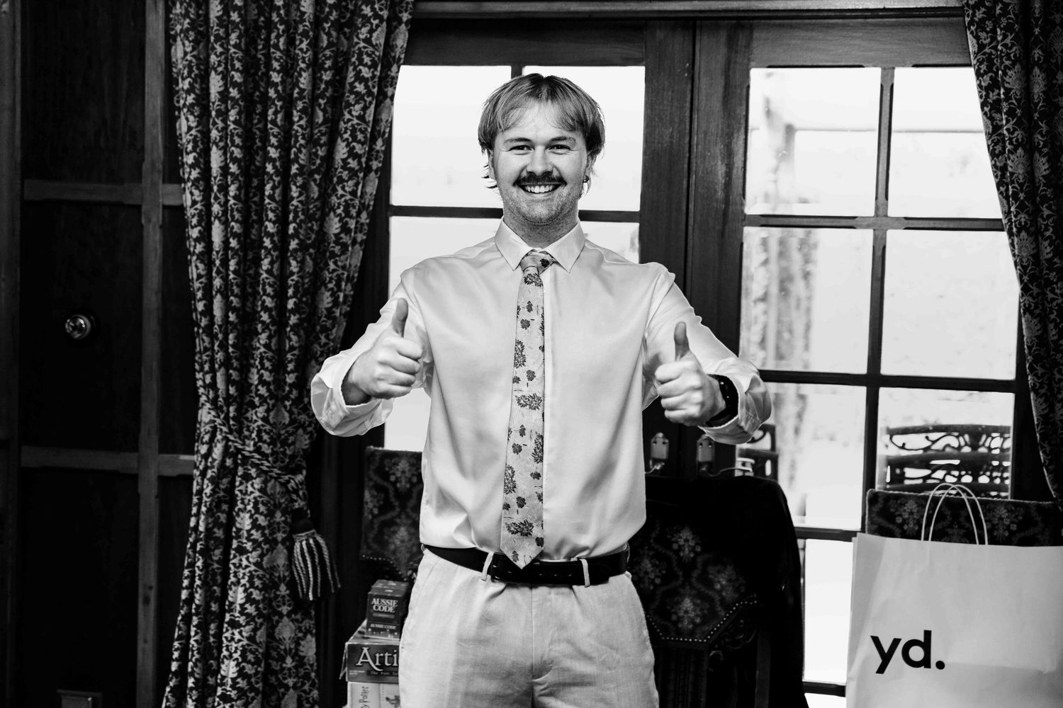 Happy groomsman in white shirt and patterned tie giving thumbs up in black and white photo.