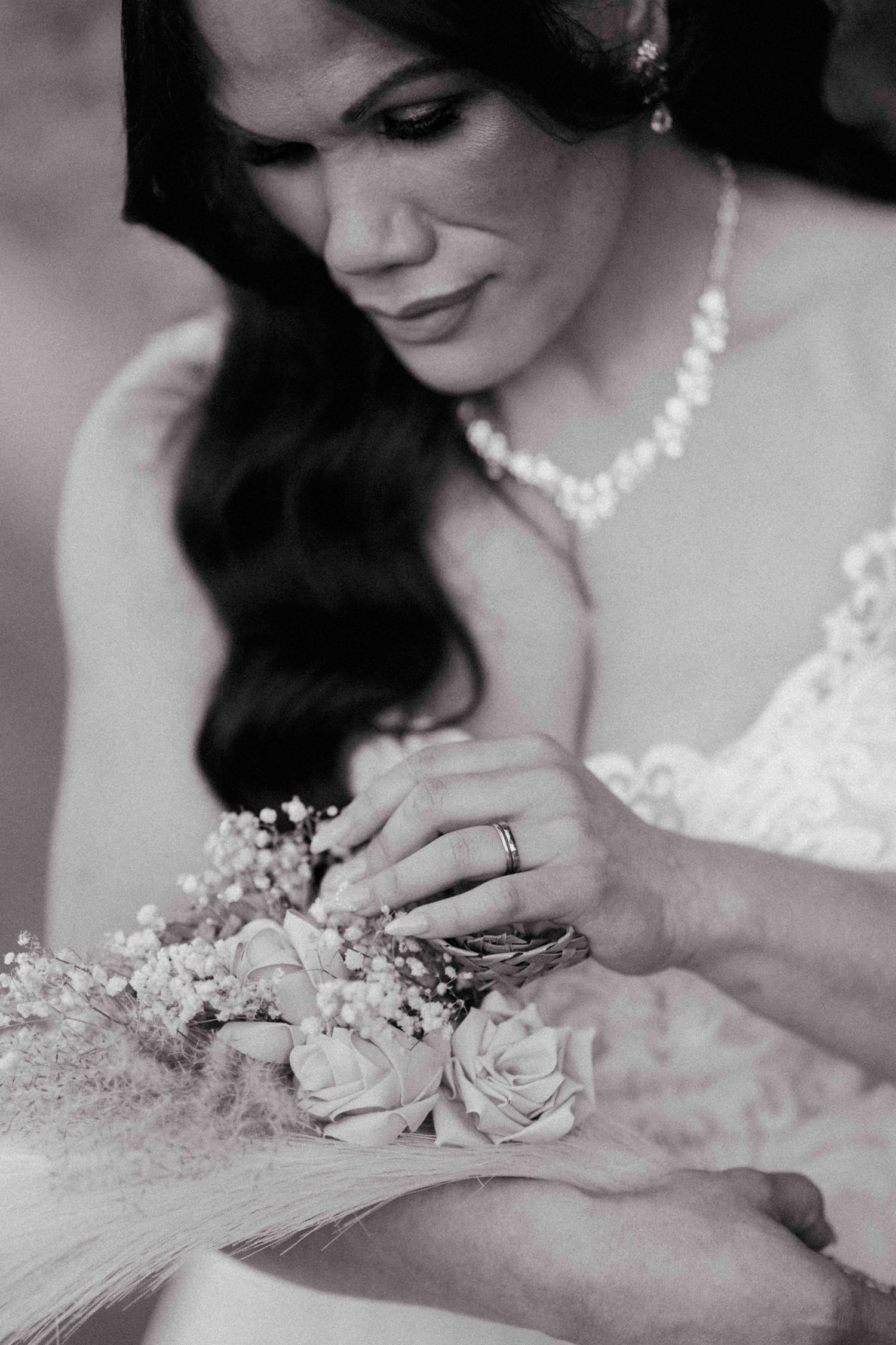 Black and white close-up of bride holding rose bouquet wearing pearl necklace.